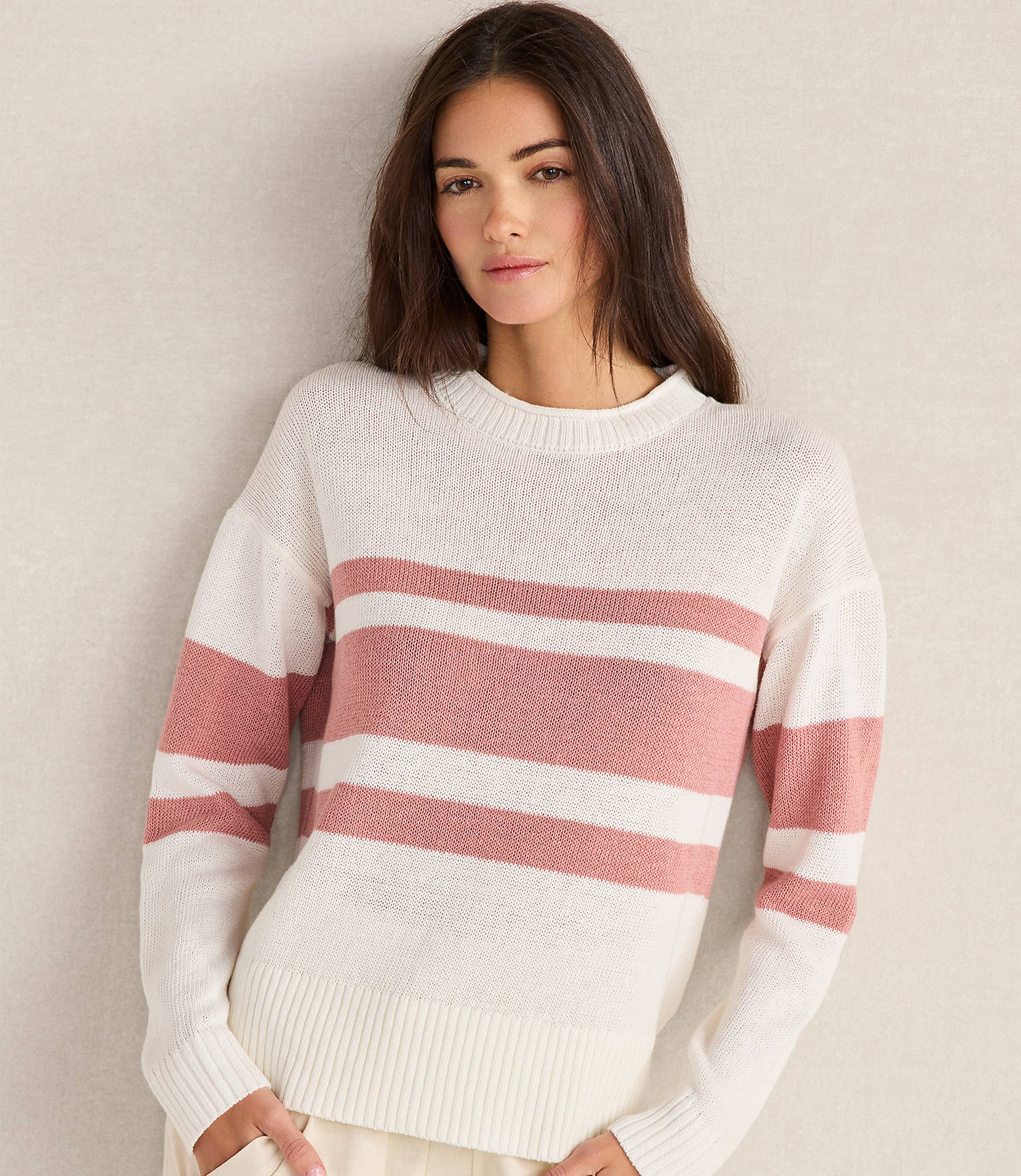 A woman in a striped sweater stands against a plain, light-colored wall.