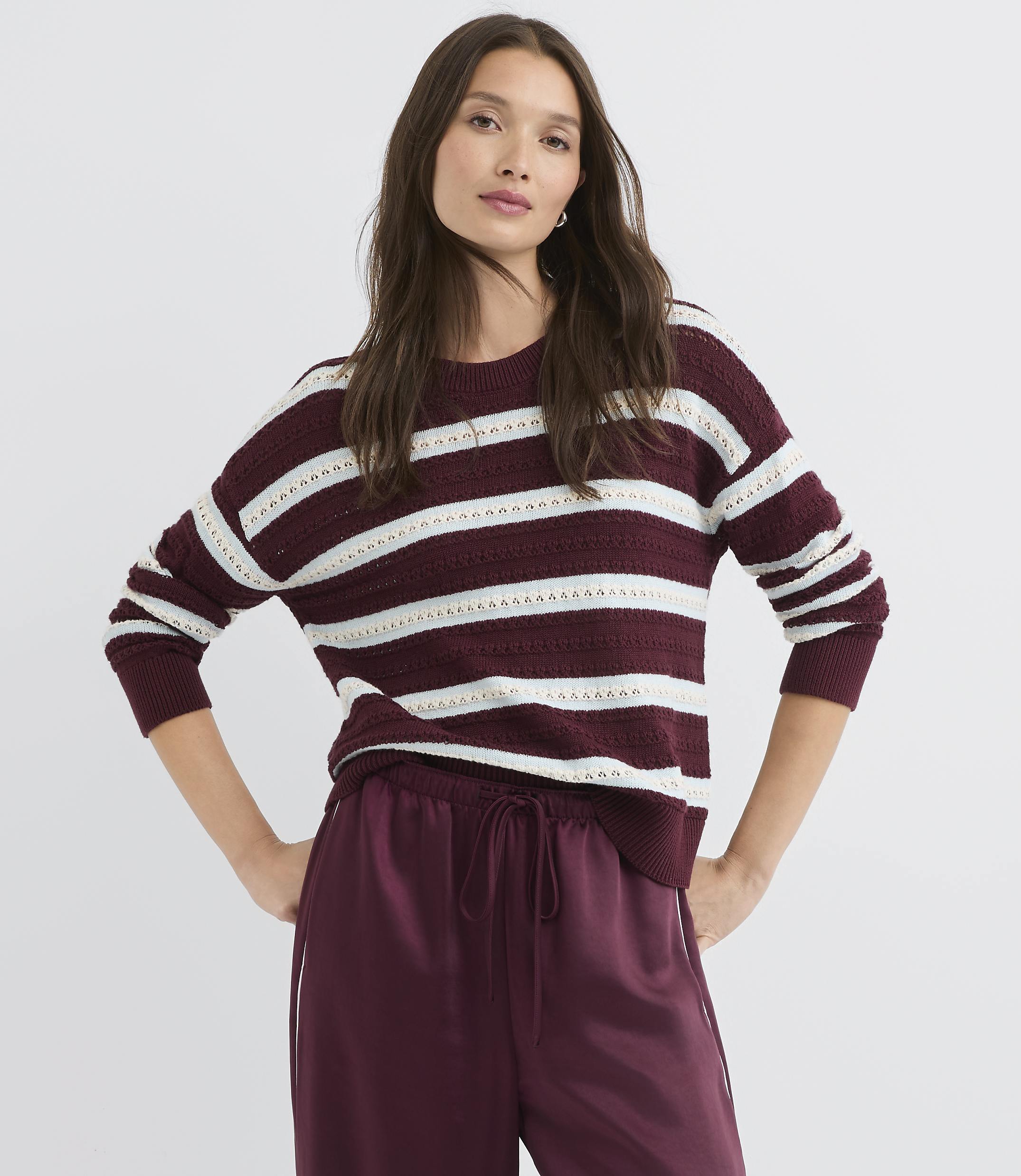 A woman in a striped sweater and satin pants stands against a plain white background.