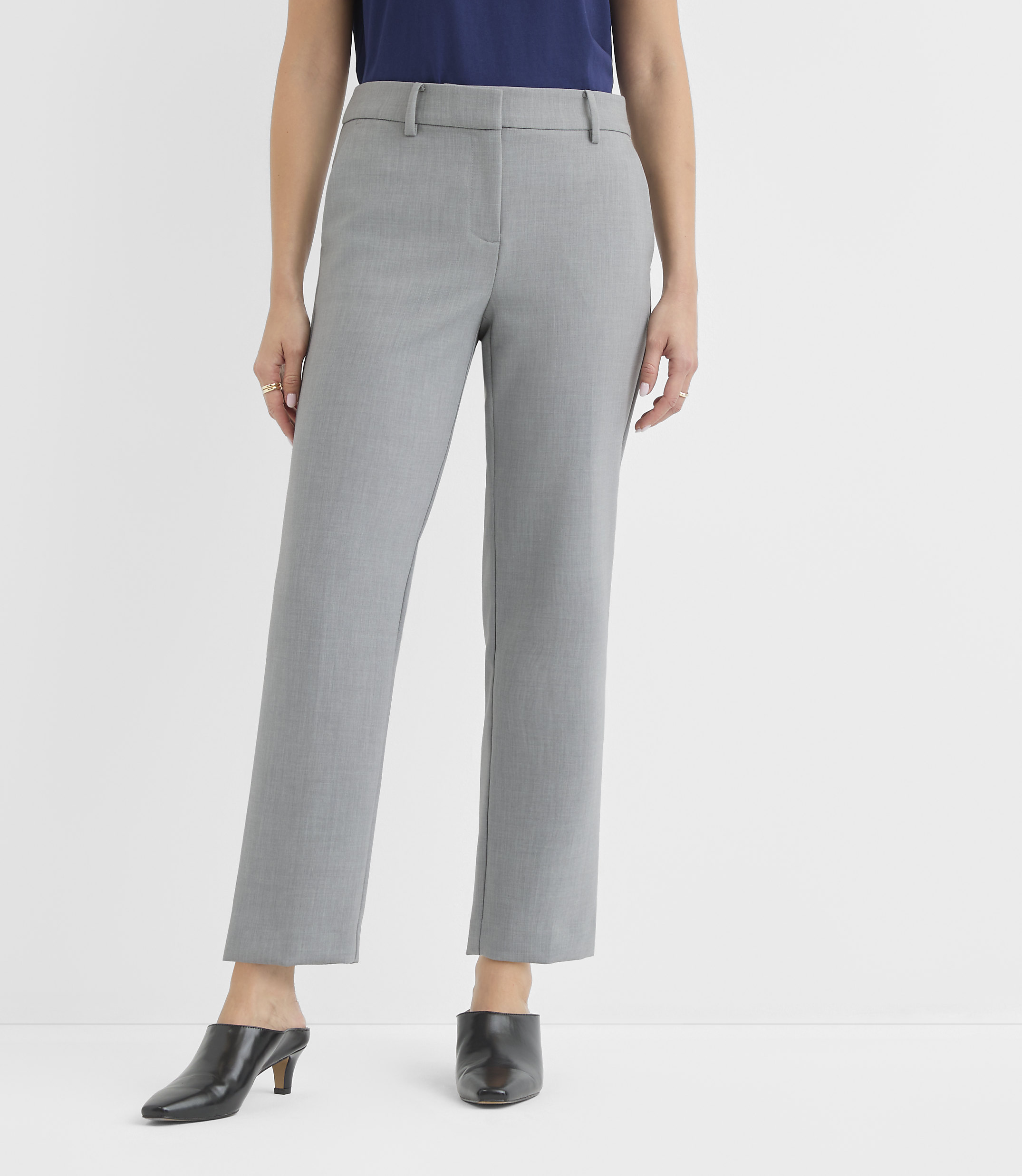 A person in gray pants and black shoes stands against a plain white background.