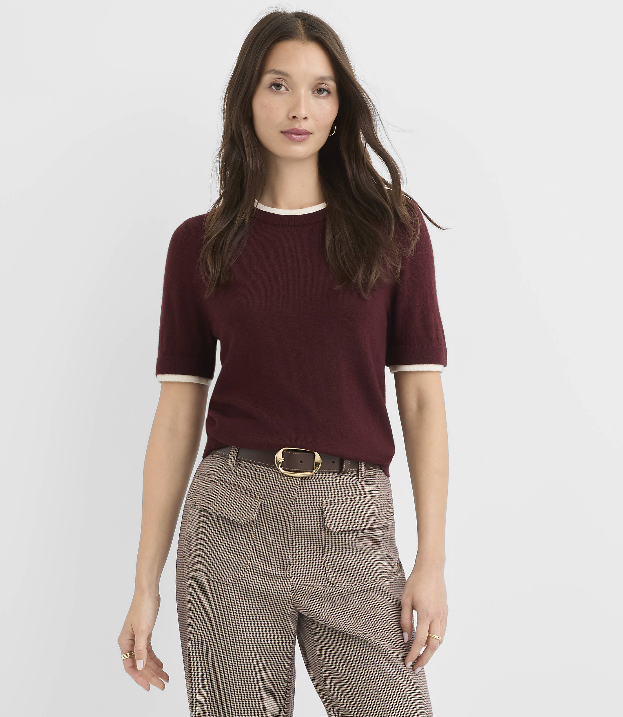 A woman in a maroon sweater and plaid pants stands against a plain white background.