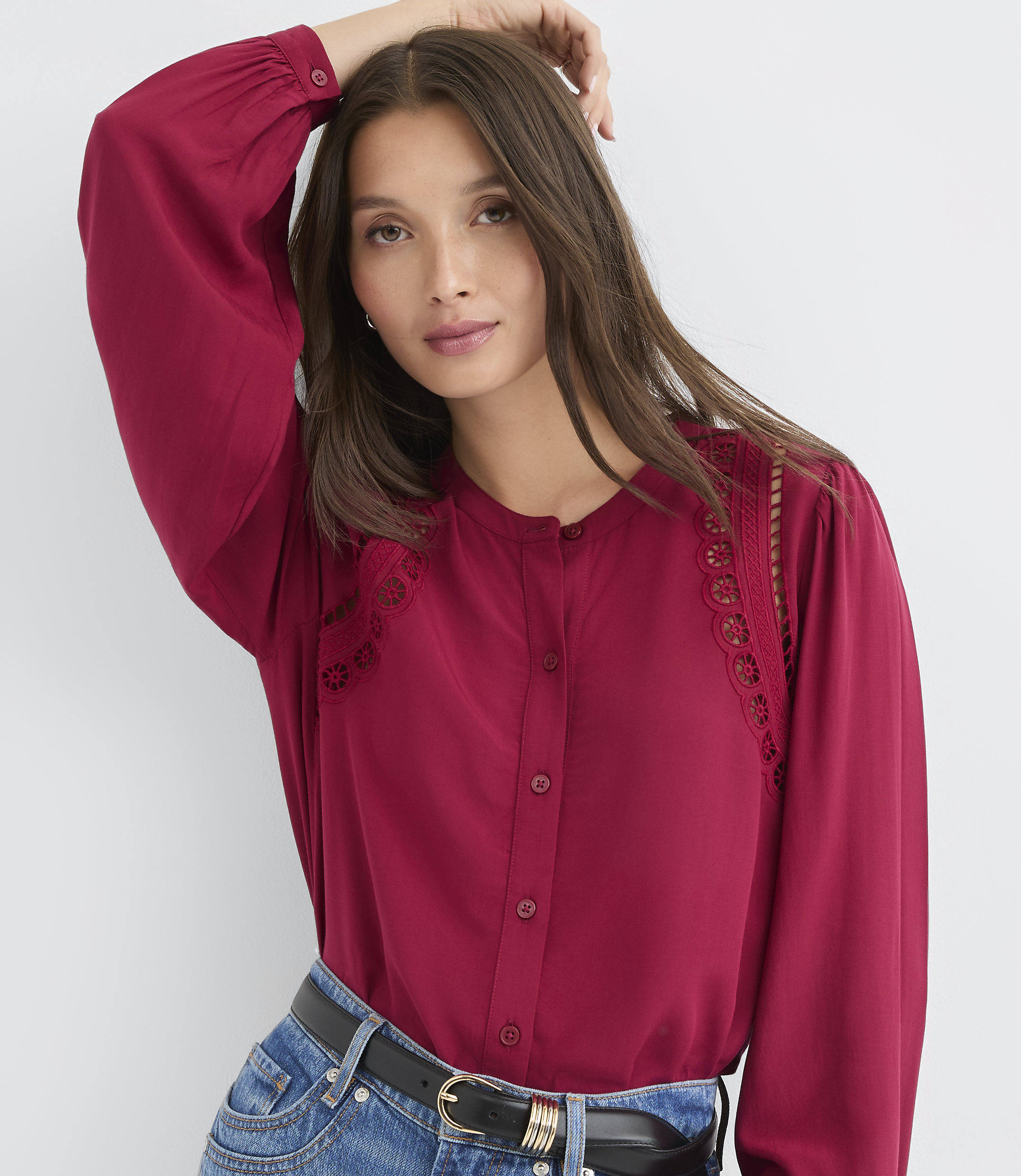 A woman in a maroon blouse and jeans poses against a plain white background.