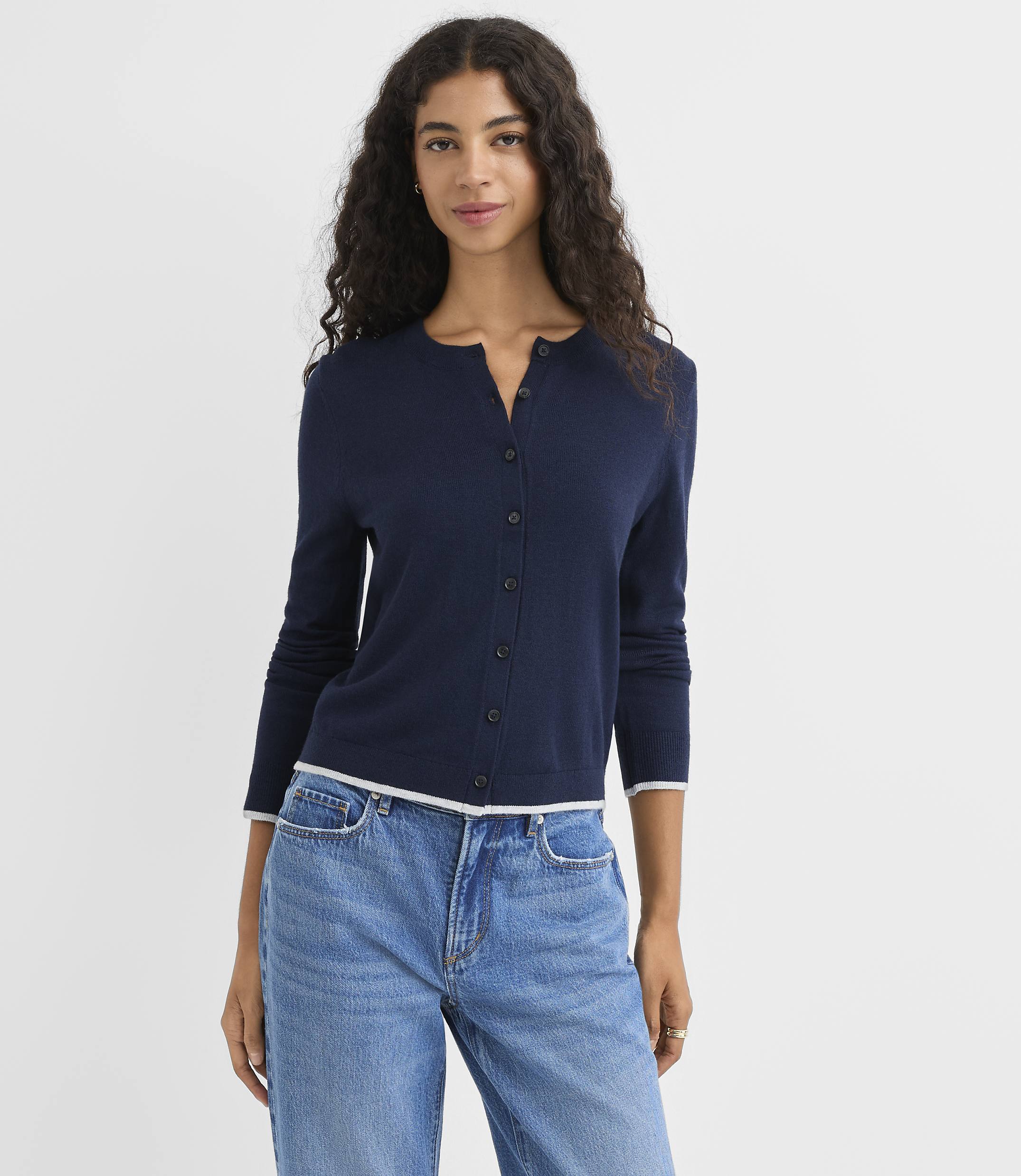 A woman in a navy cardigan and blue jeans stands against a plain white background.