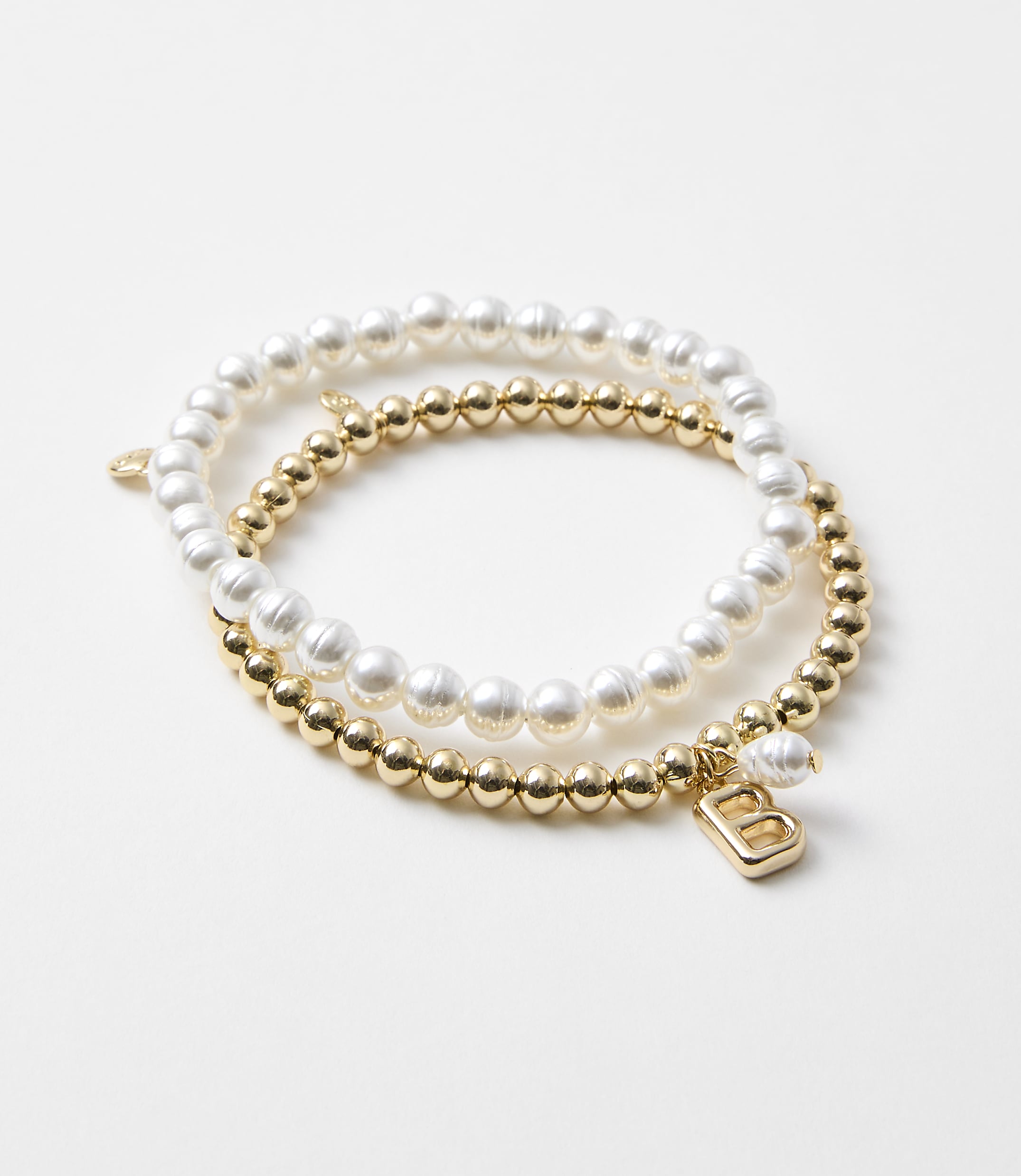 Two bracelets, one with pearls and the other with gold beads and a charm, rest on a plain white background.