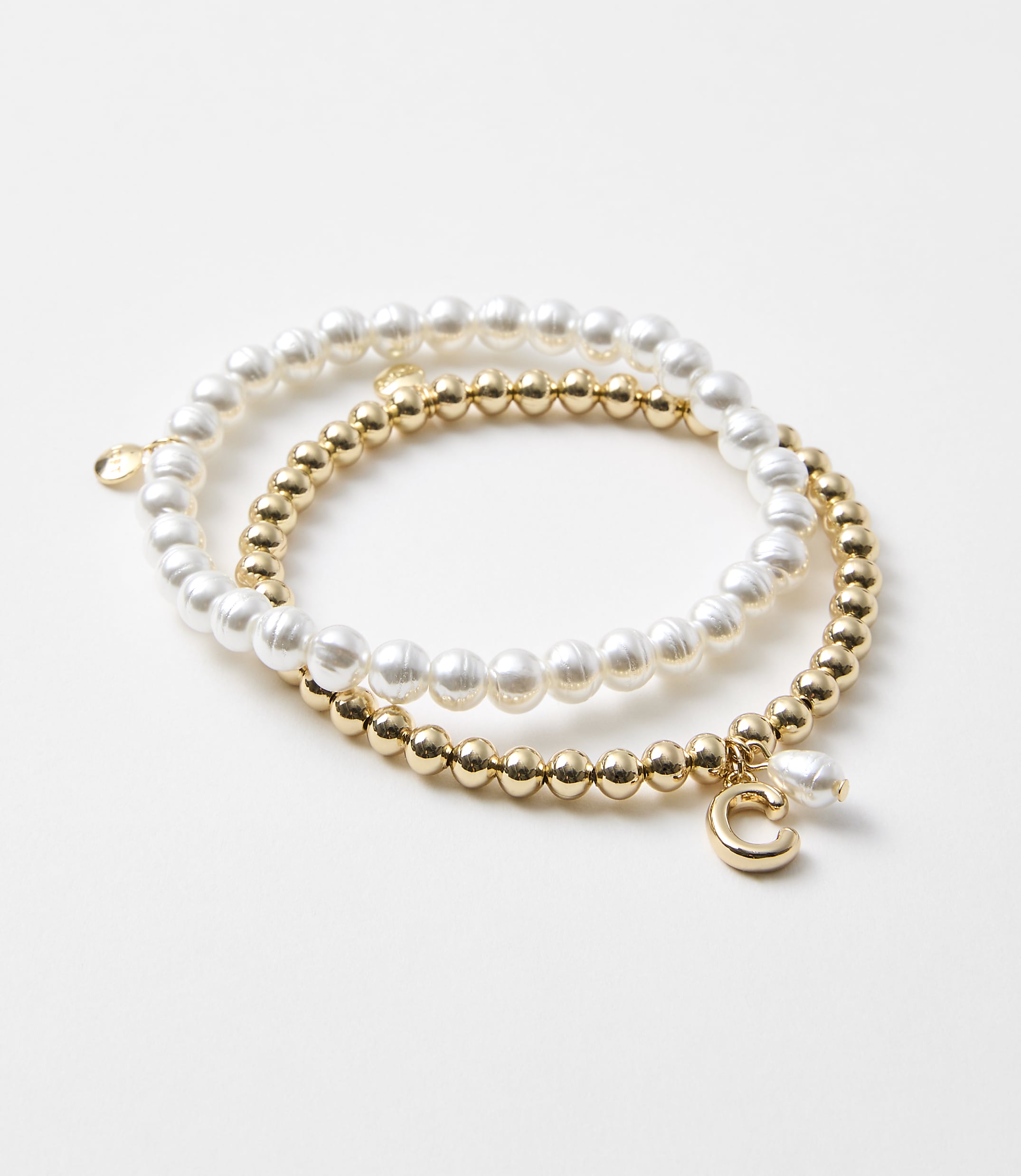 Two bracelets, one with pearls and the other with gold beads and a charm, rest on a plain white background.