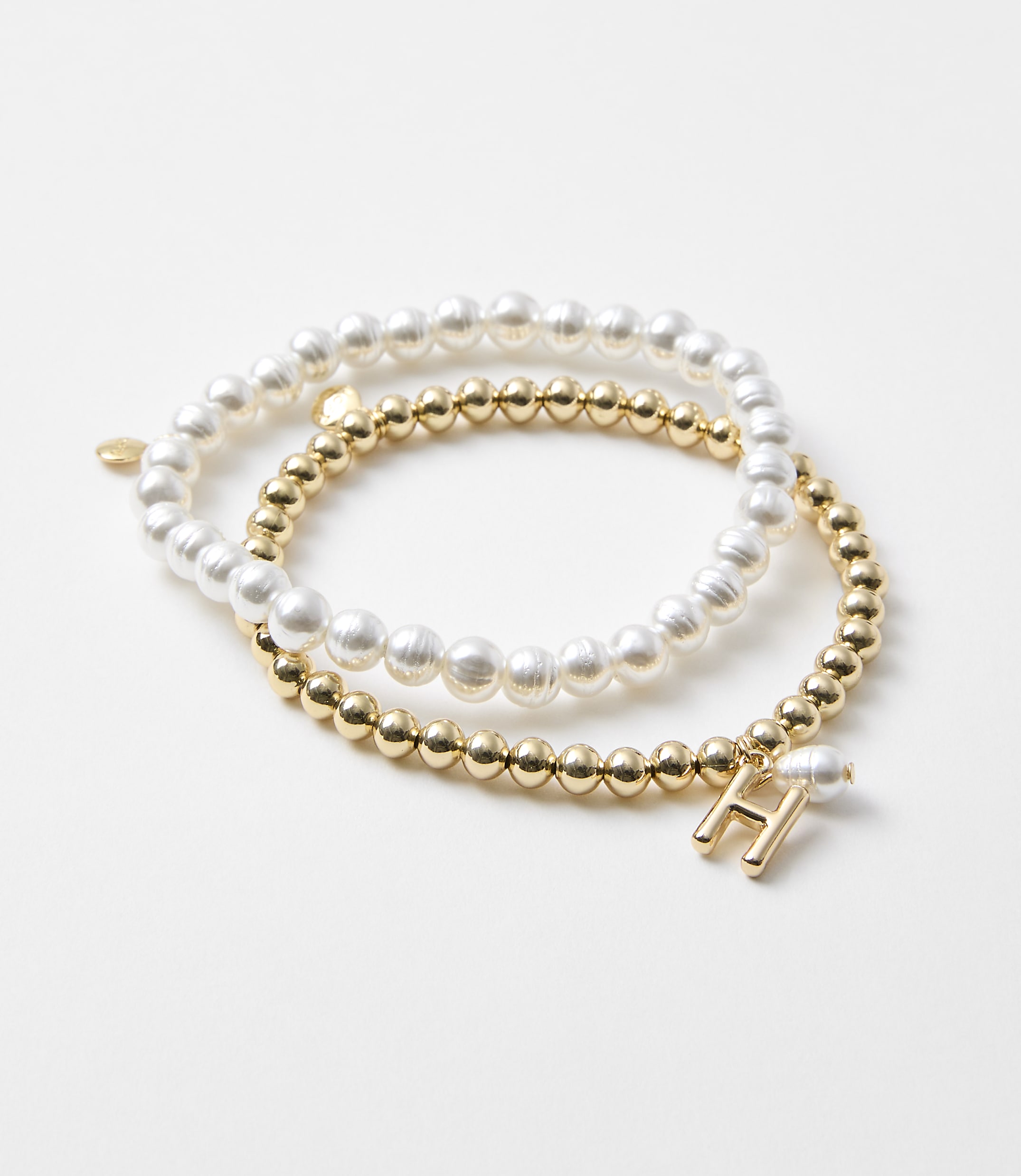 Two bracelets, one with pearls and the other with gold beads and an "H" charm, rest on a plain white background.