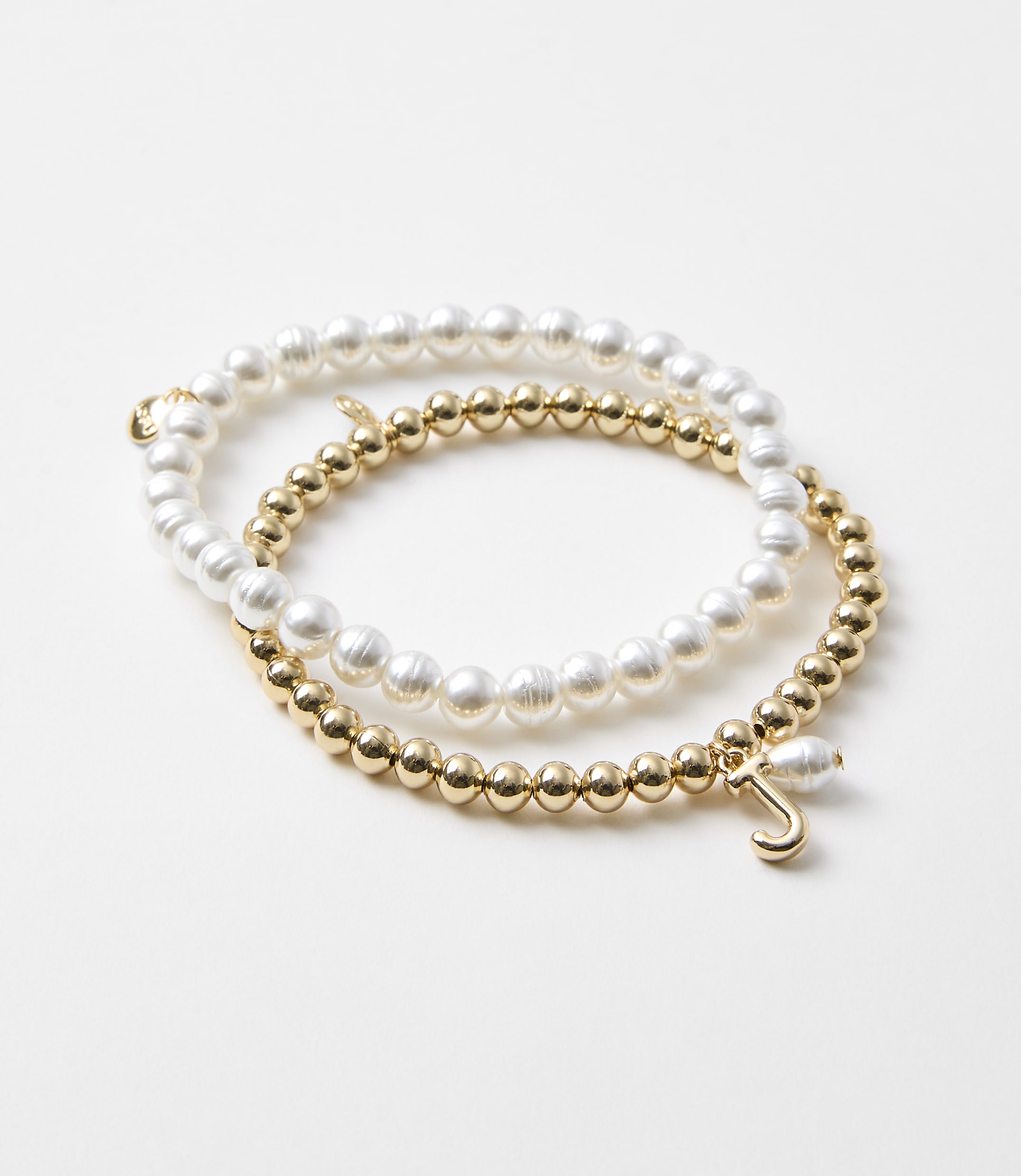 Two bracelets, one with pearls and the other with gold beads and a charm, rest on a plain white background.