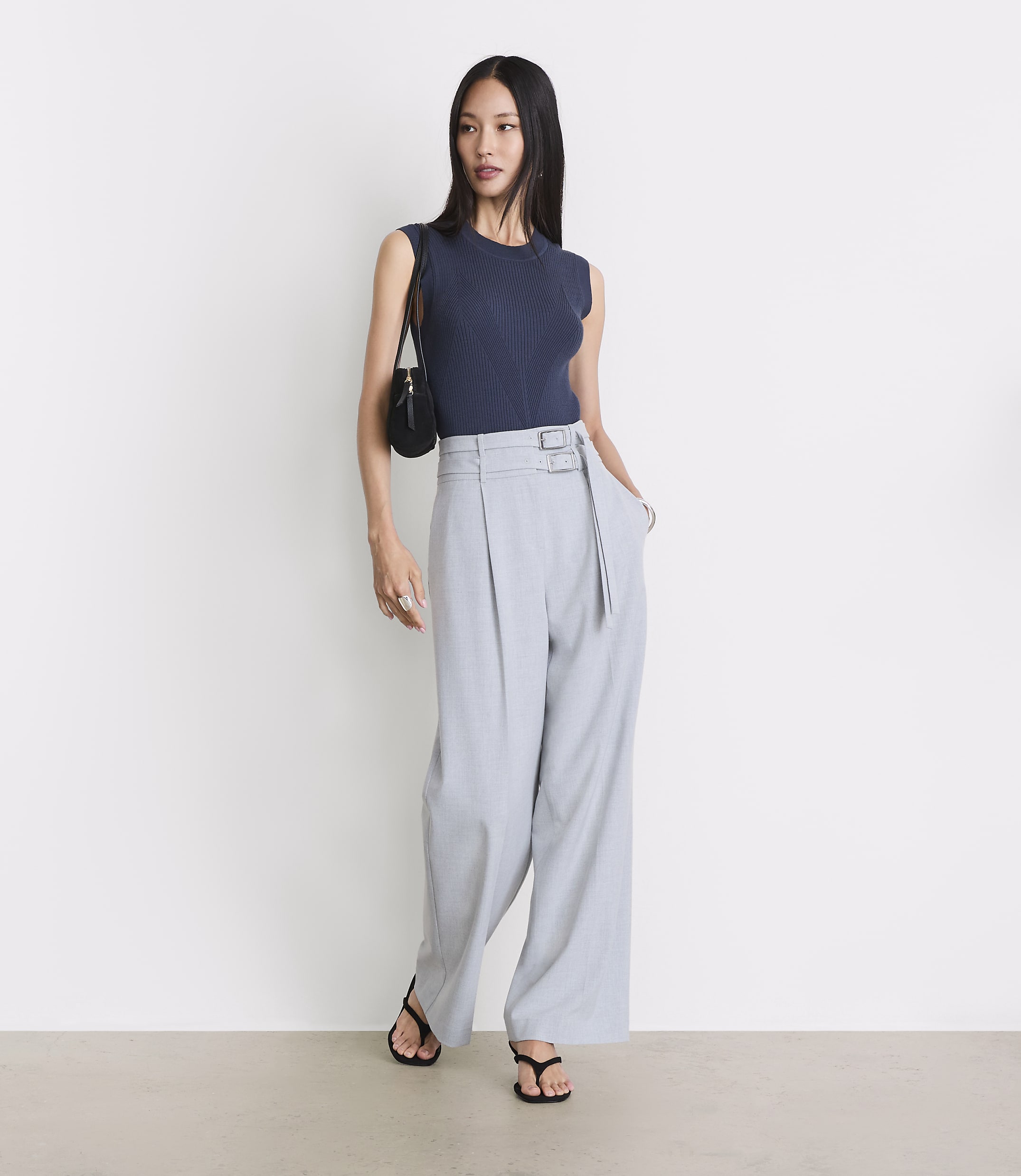 A woman in a navy top and light gray wide-leg pants stands against a plain white background.