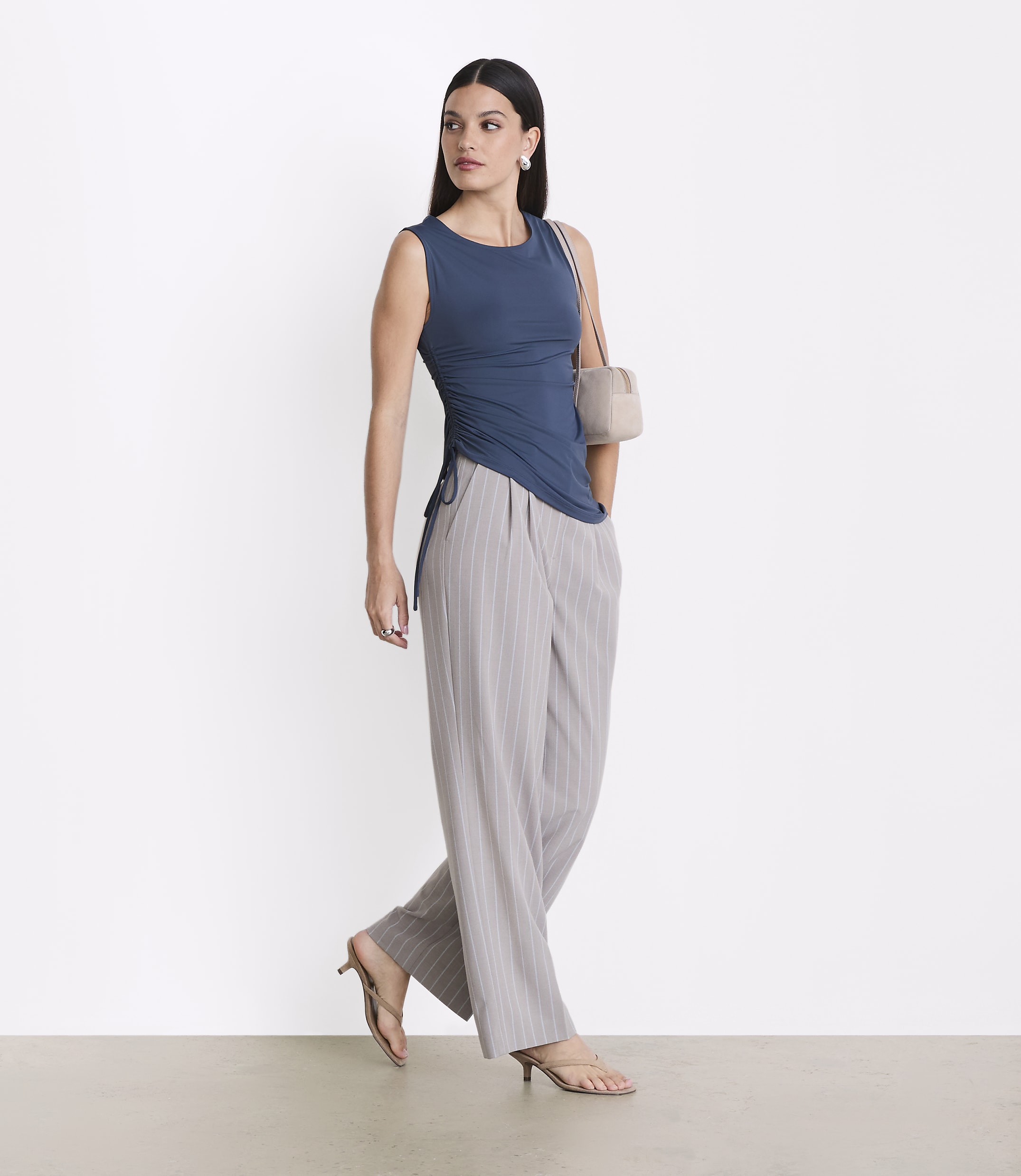 A woman in a blue top and striped pants stands against a plain white background.