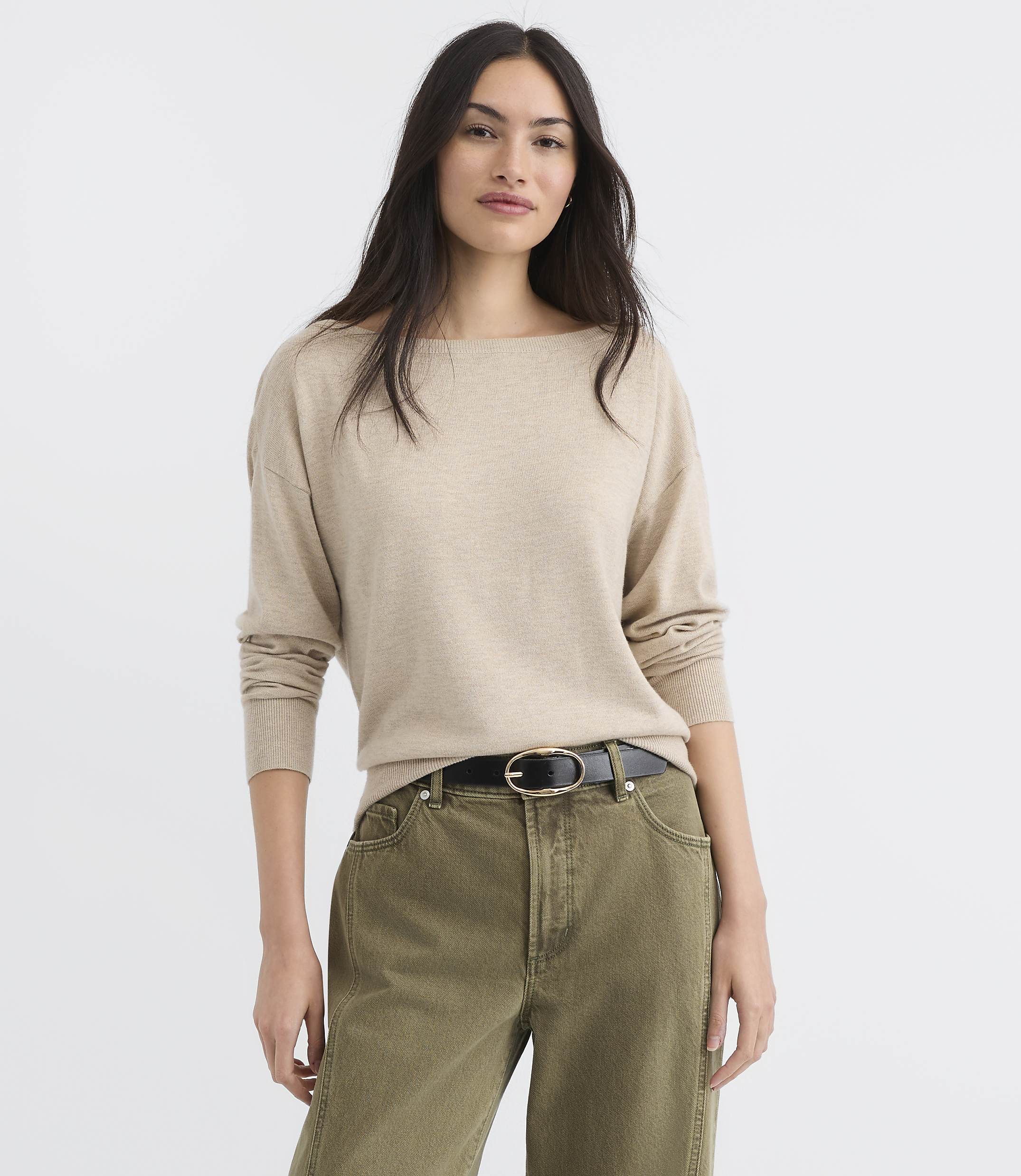 A woman in a beige sweater and green pants stands against a plain white background.