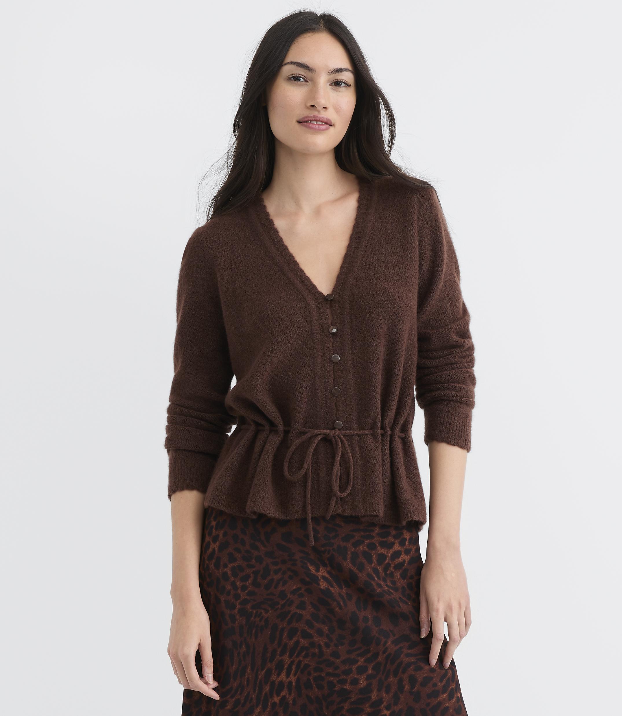 A woman in a brown cardigan and leopard print skirt stands against a plain white background.