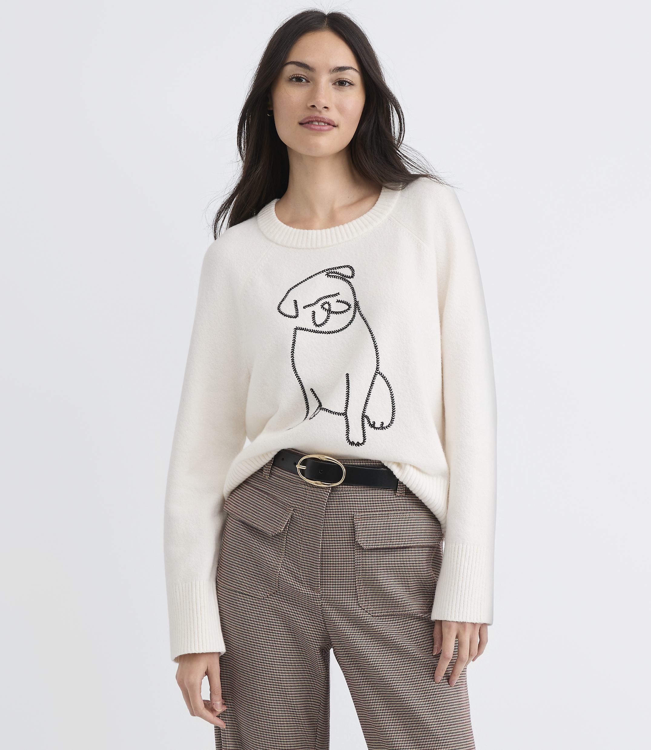 A woman in a cream sweater with a pug design stands against a plain white background.