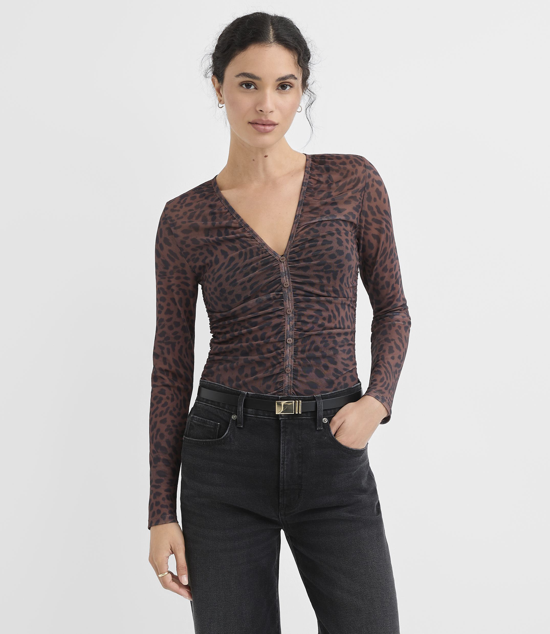 A woman in a sheer leopard print top and black jeans stands against a plain white background.