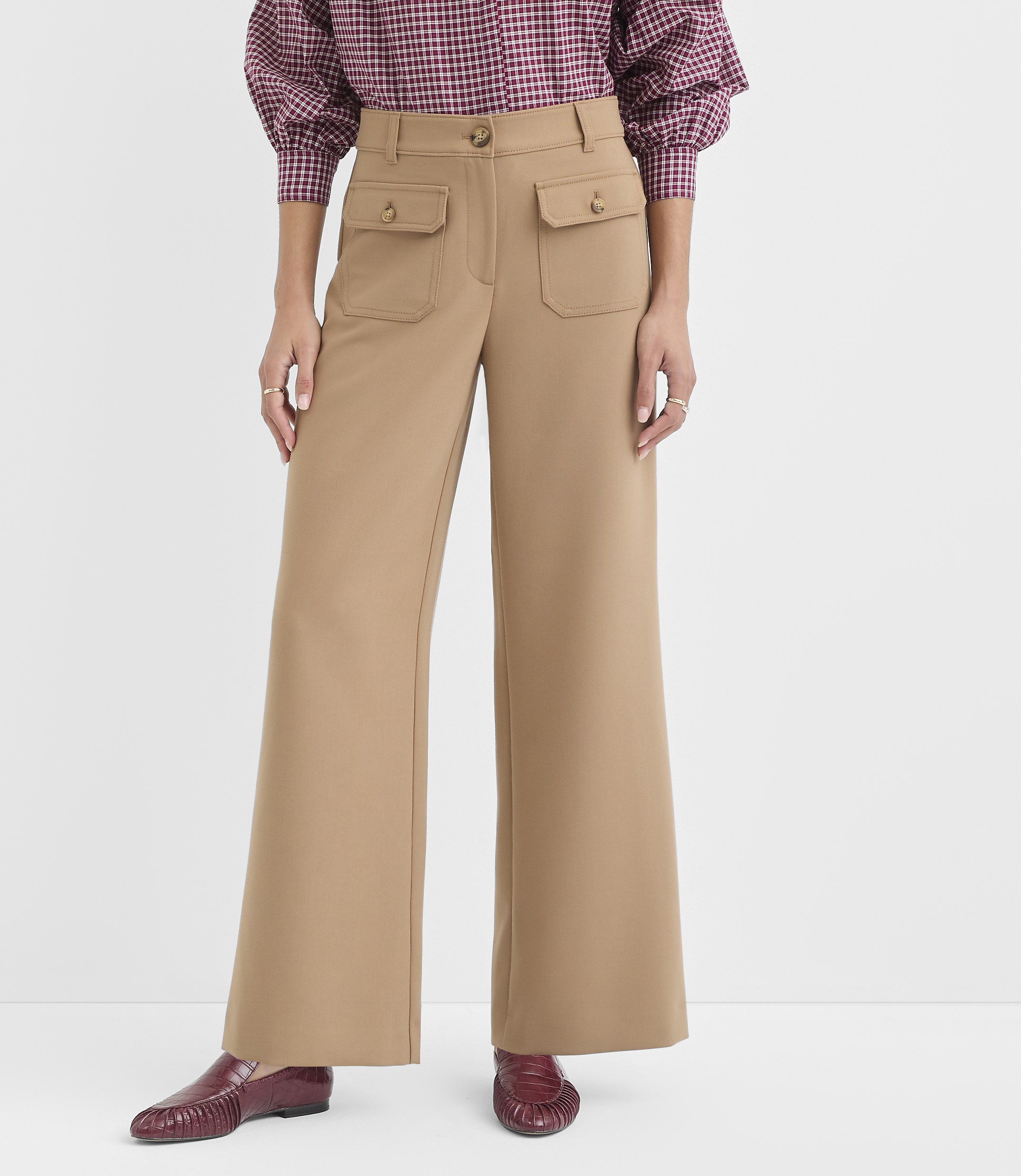 A person stands in tan wide-leg pants with pocket details and burgundy loafers, against a plain white background.