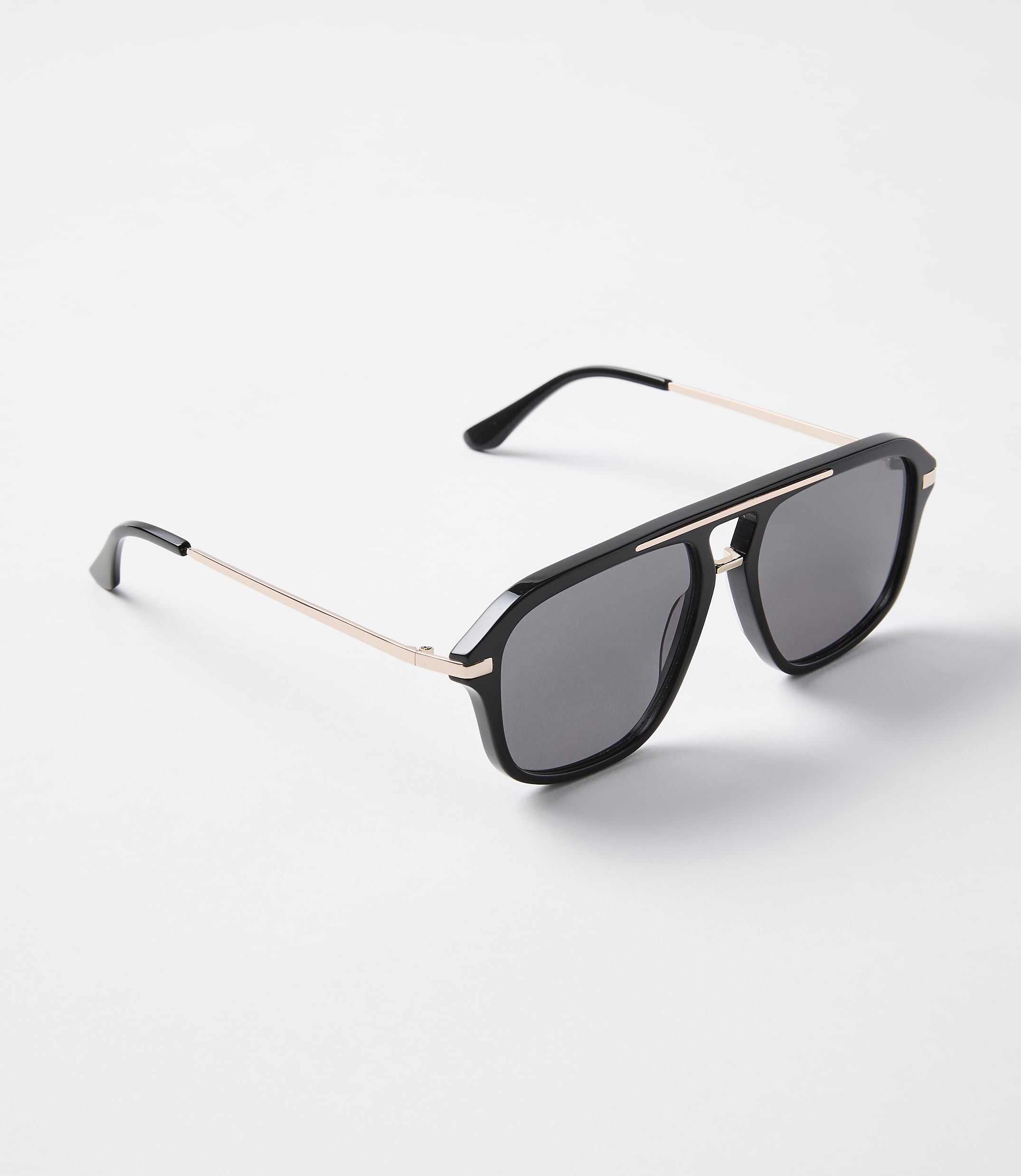 A pair of black aviator sunglasses with rose gold accents rests on a plain white background.