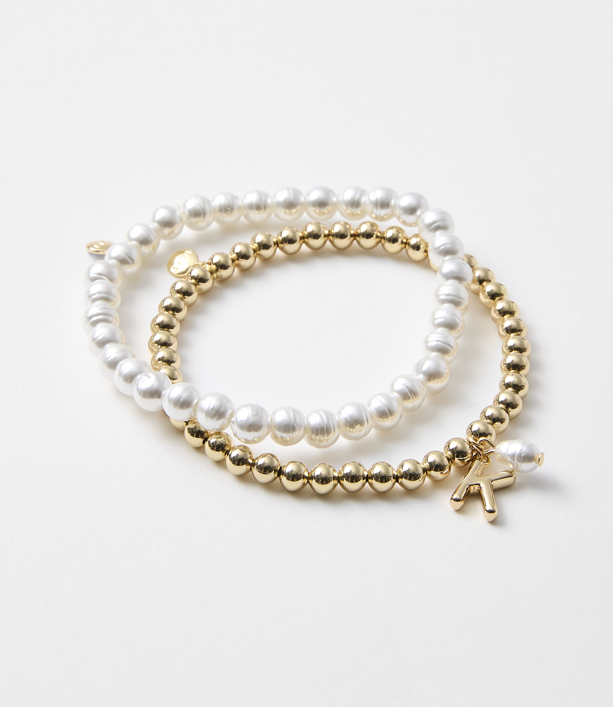 Two bracelets, one with pearls and the other with gold beads and a charm, rest on a plain white background.