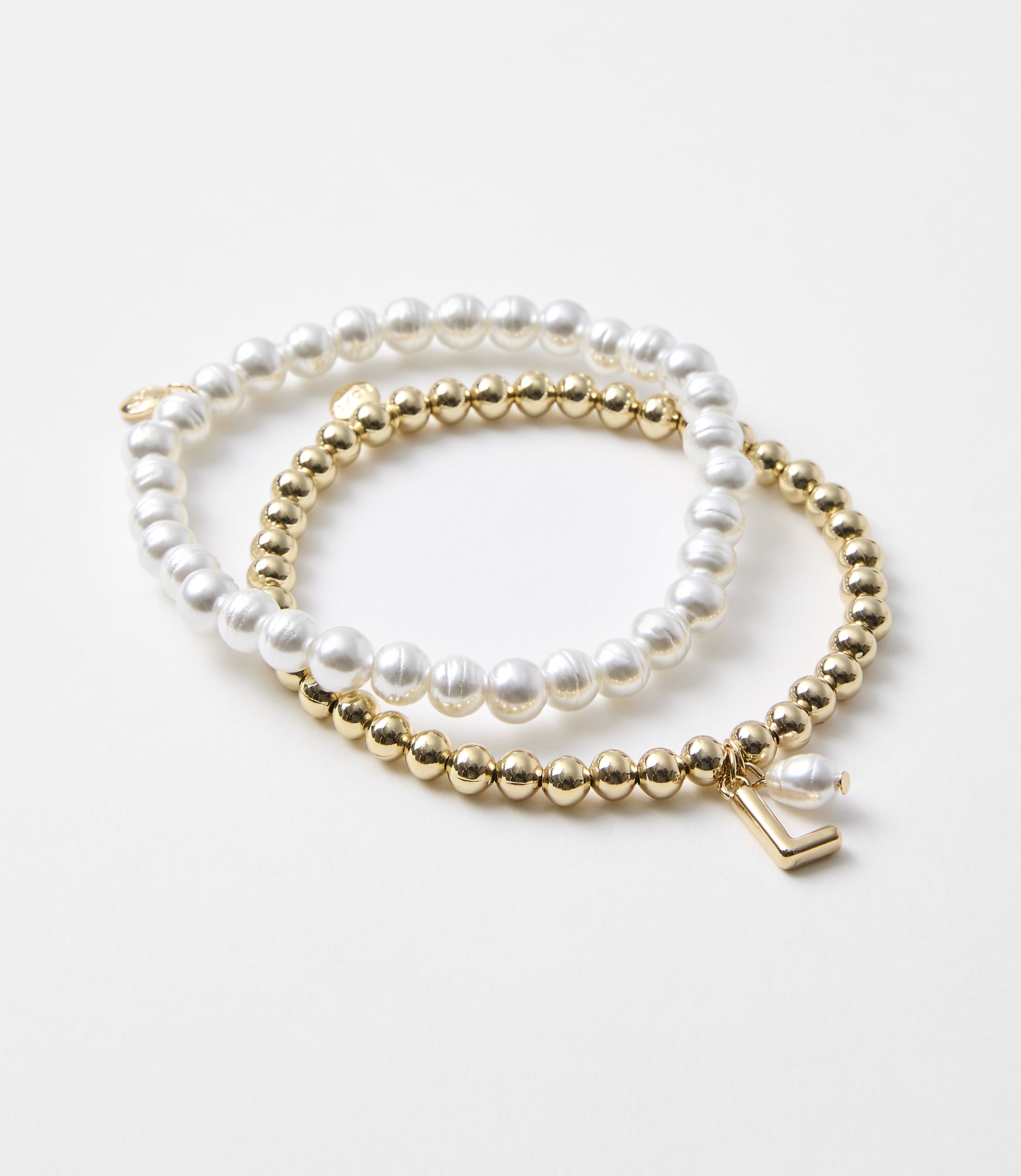 Two bracelets, one with pearls and the other with gold beads and a charm, rest on a plain white background.