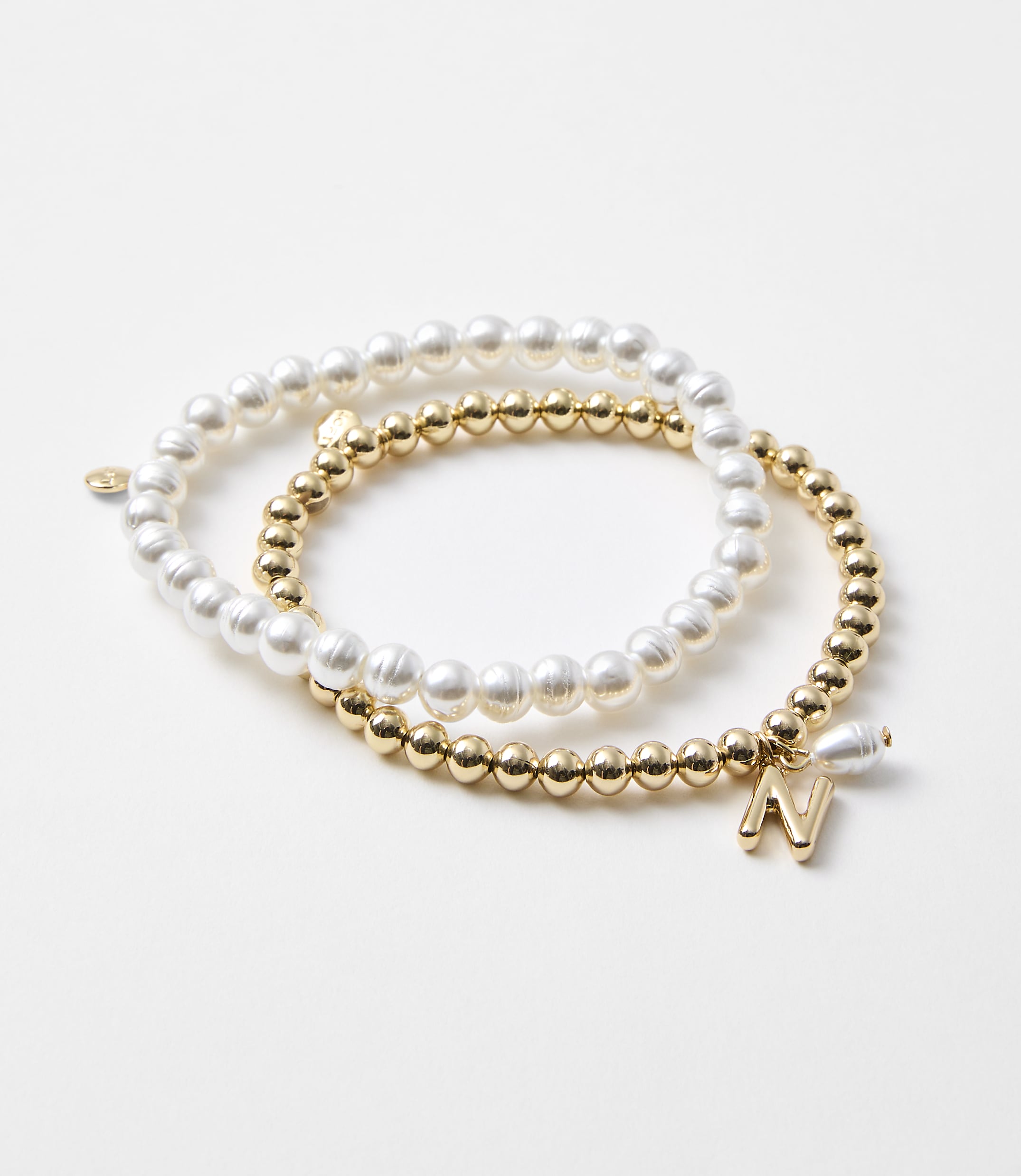 Two bracelets, one with pearls and the other with gold beads and an initial charm, rest on a plain white background.