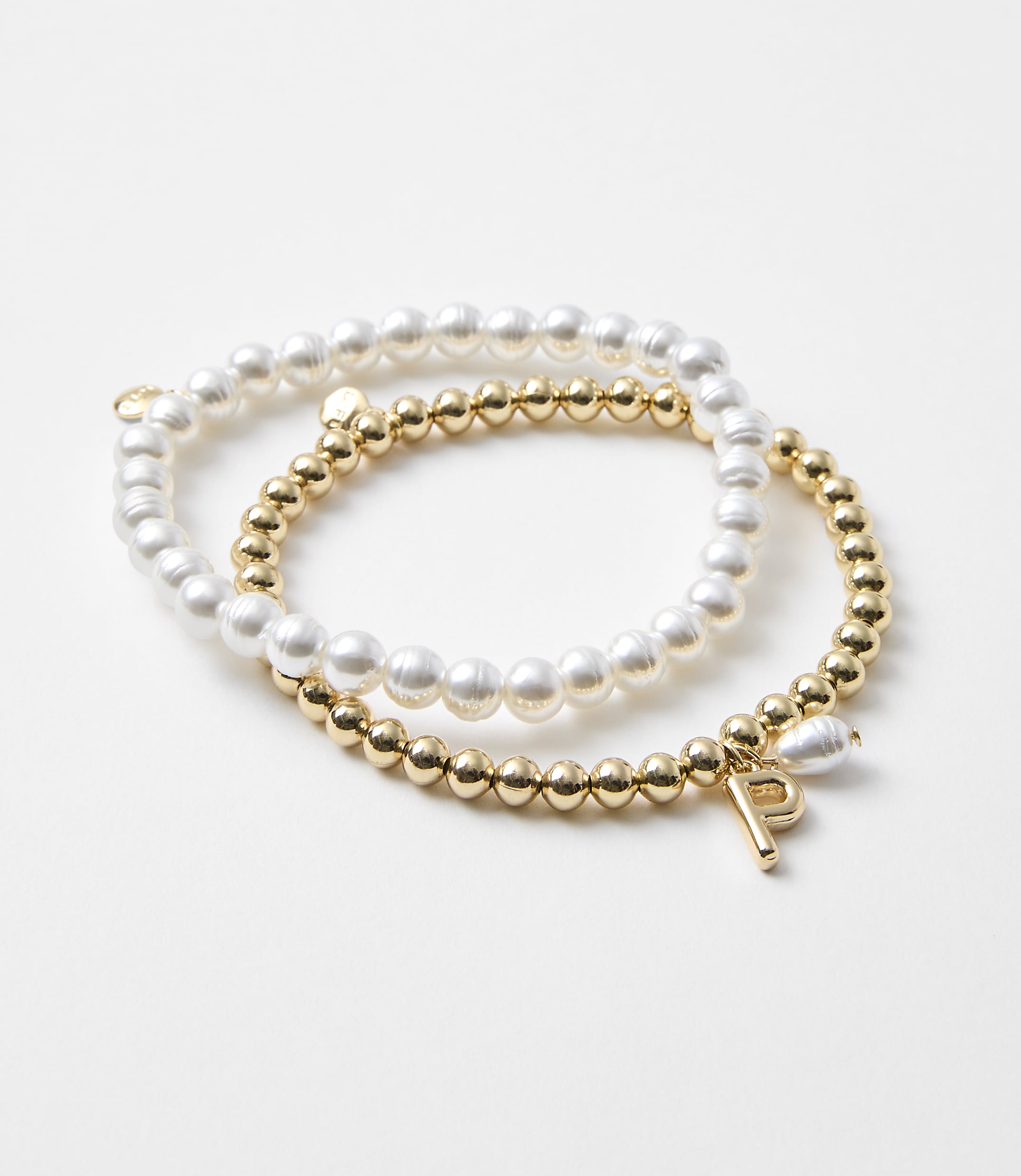 Two bracelets, one with pearls and the other with gold beads and a charm, rest on a plain white background.