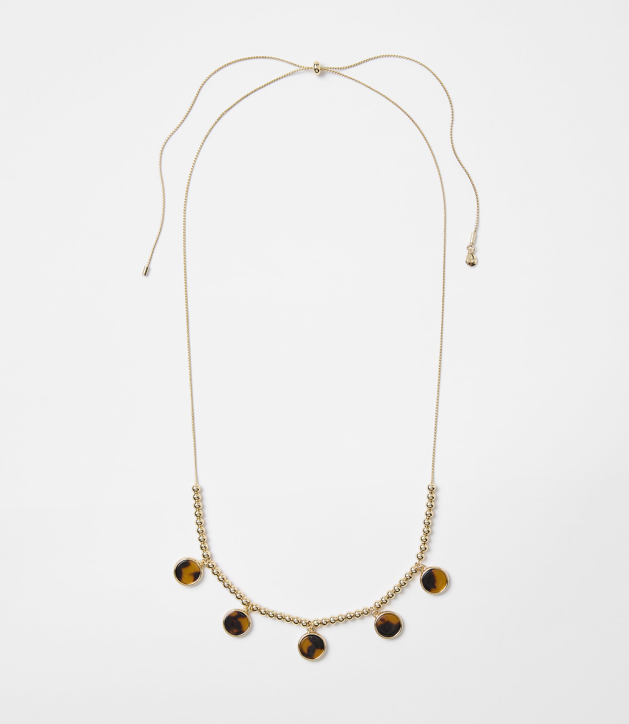 A delicate gold necklace with small beads and tortoise shell pendants hangs against a plain white background.