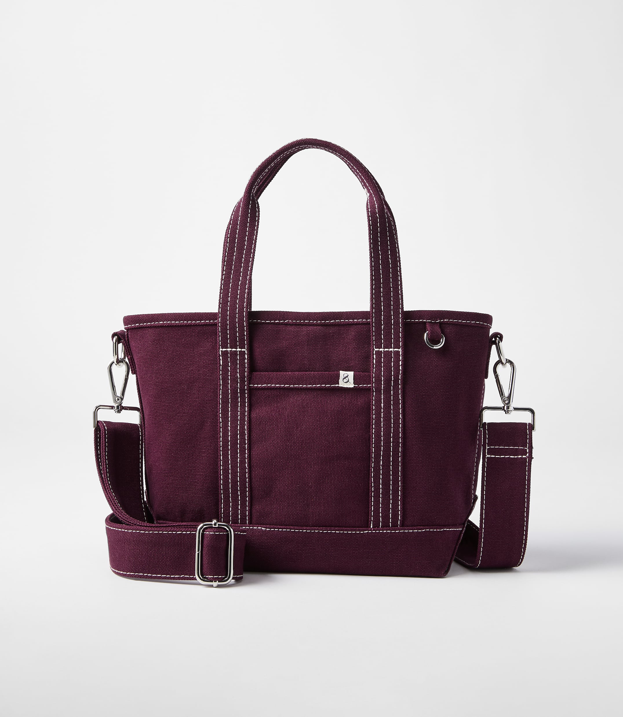 A burgundy canvas tote bag with white stitching and a detachable shoulder strap rests on a white background.