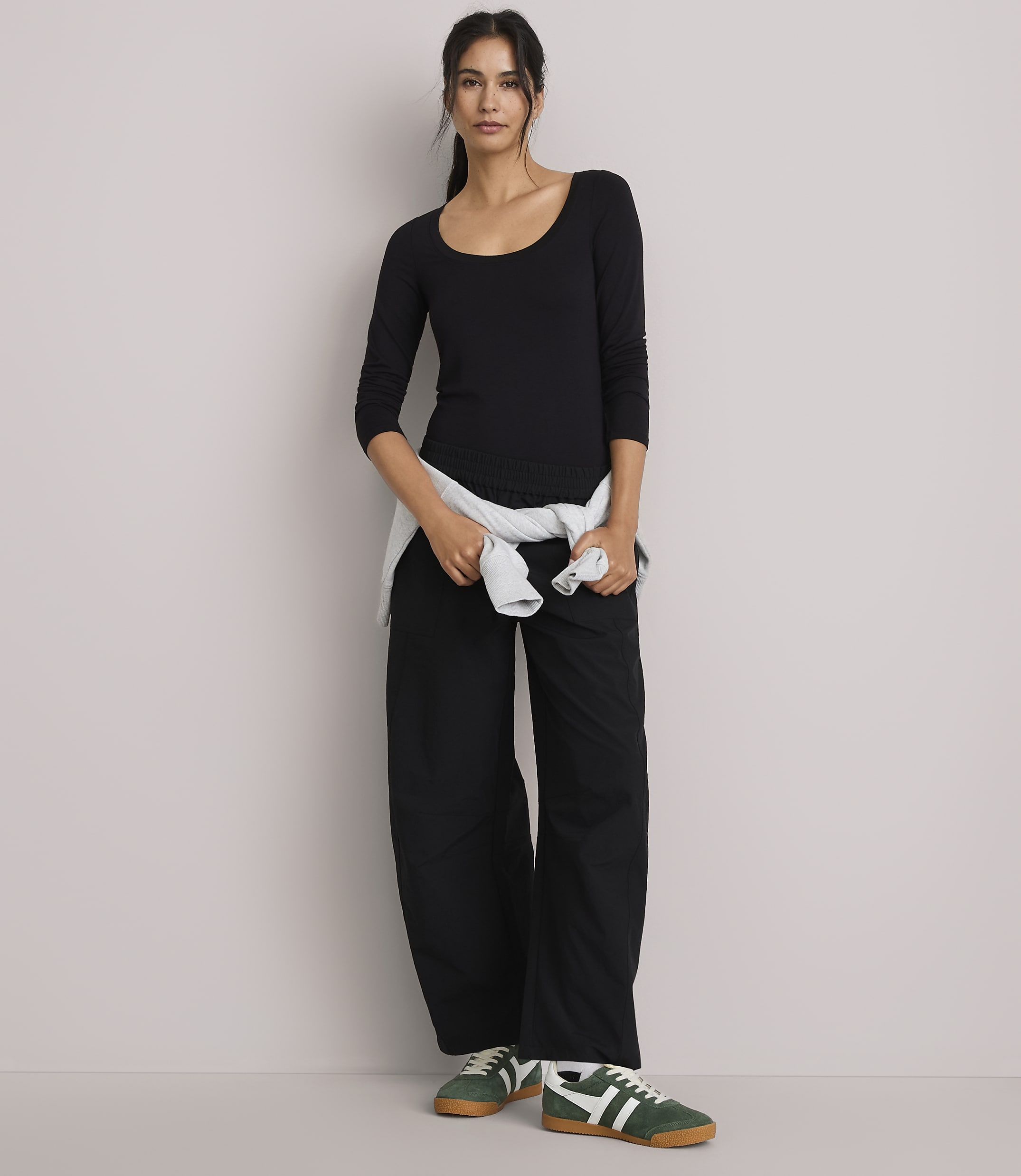 A woman in a black top and wide-leg pants stands against a plain, light-colored wall.