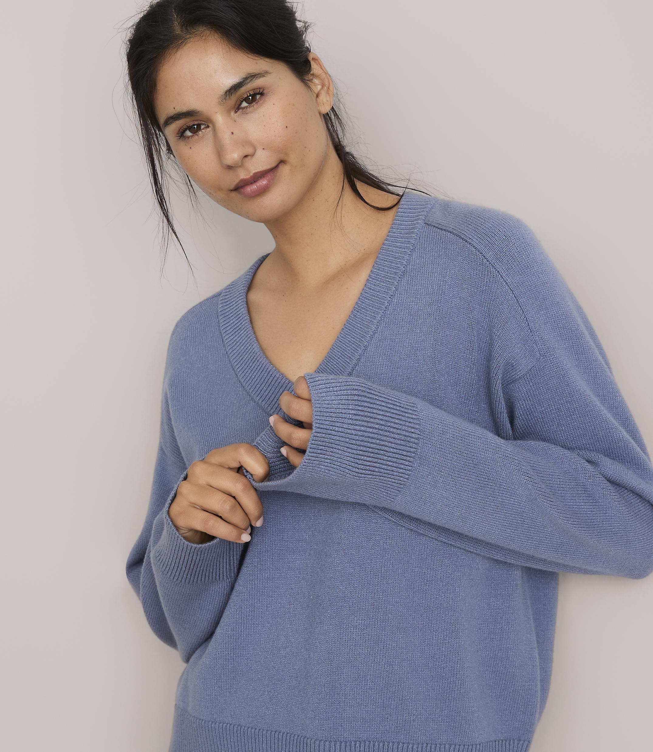 A woman in a blue v-neck sweater poses against a plain, light gray background.