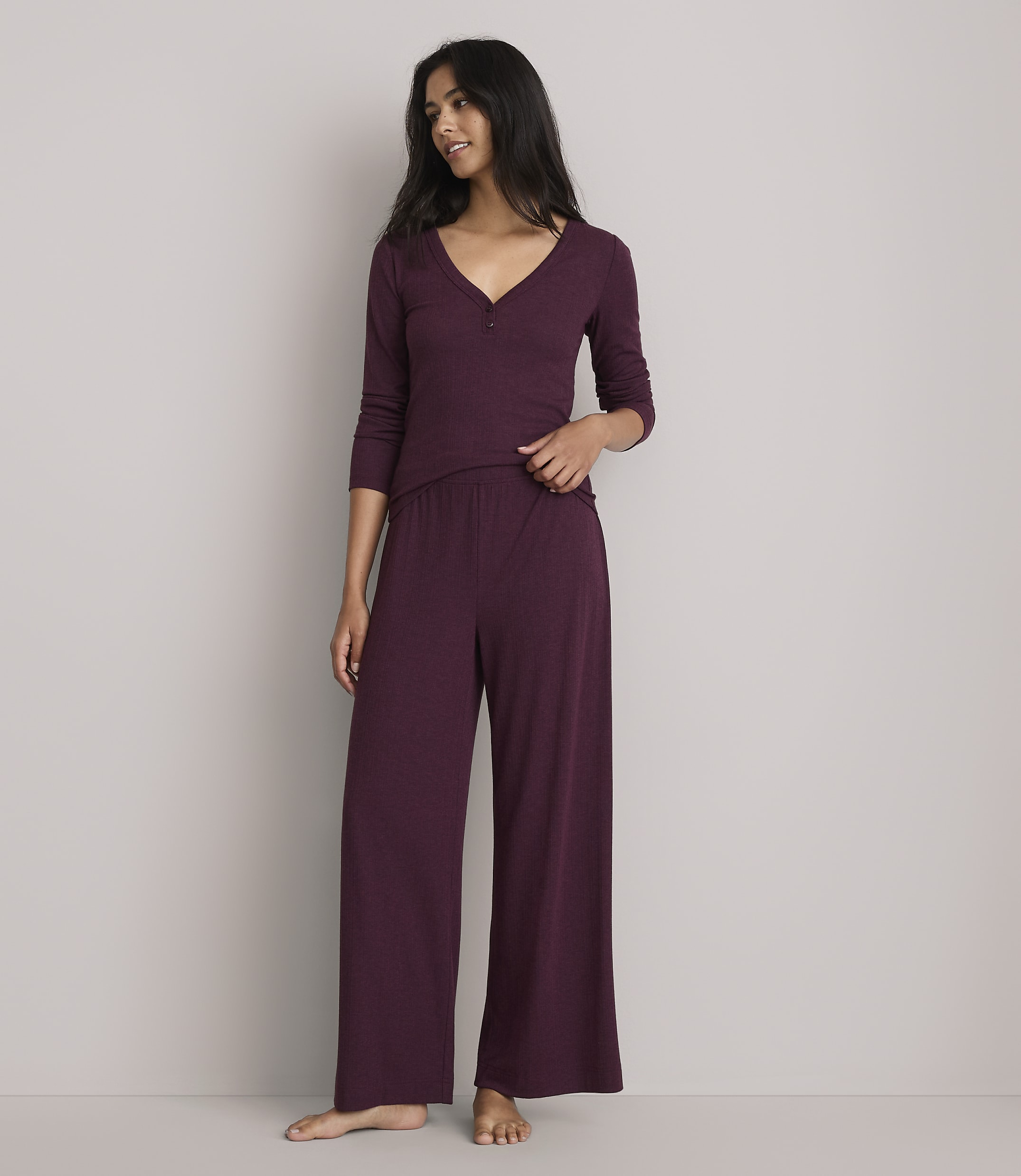 A woman in burgundy pajamas stands against a plain gray background.