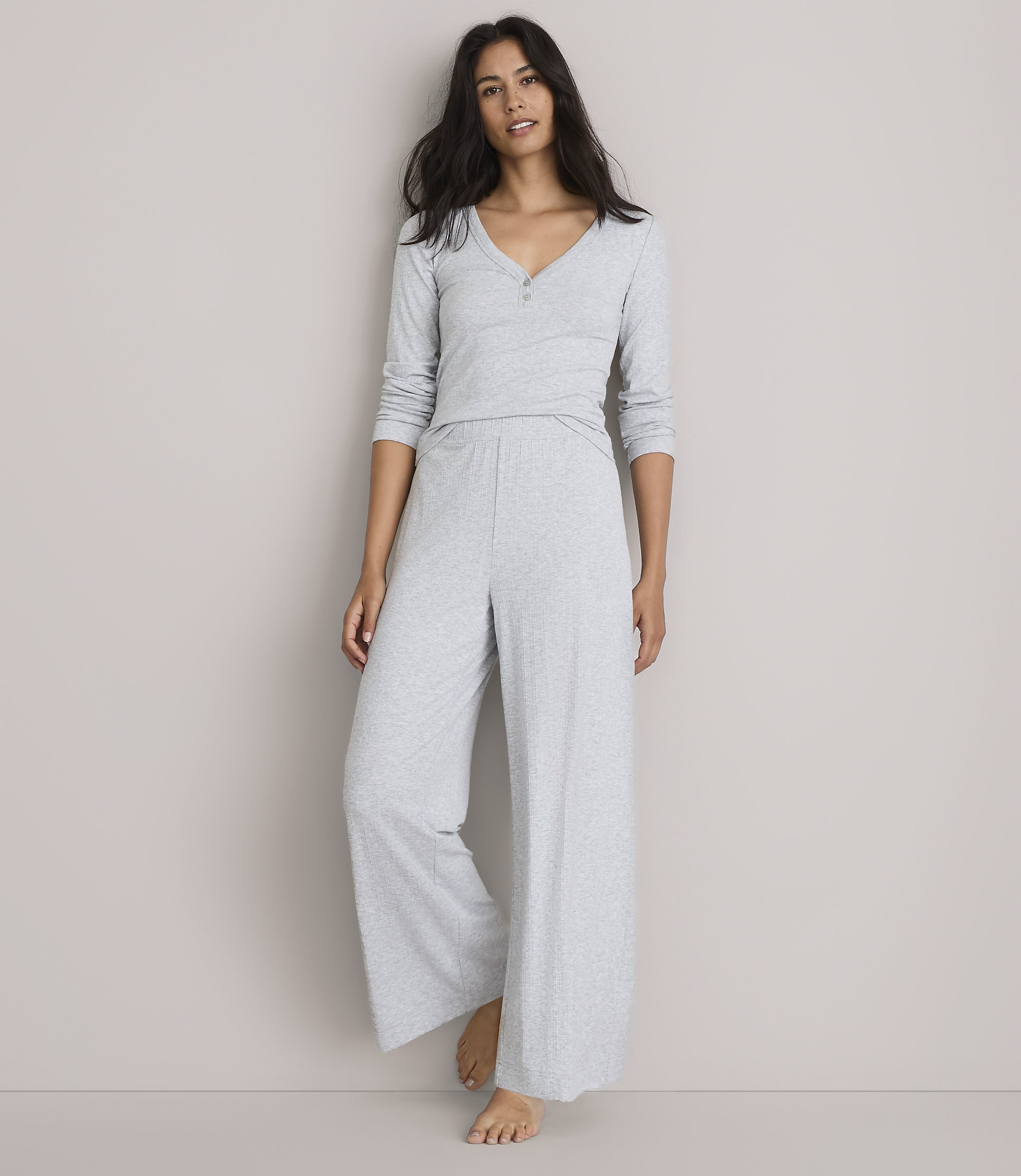 A woman in light gray pajamas stands against a plain, light gray background.