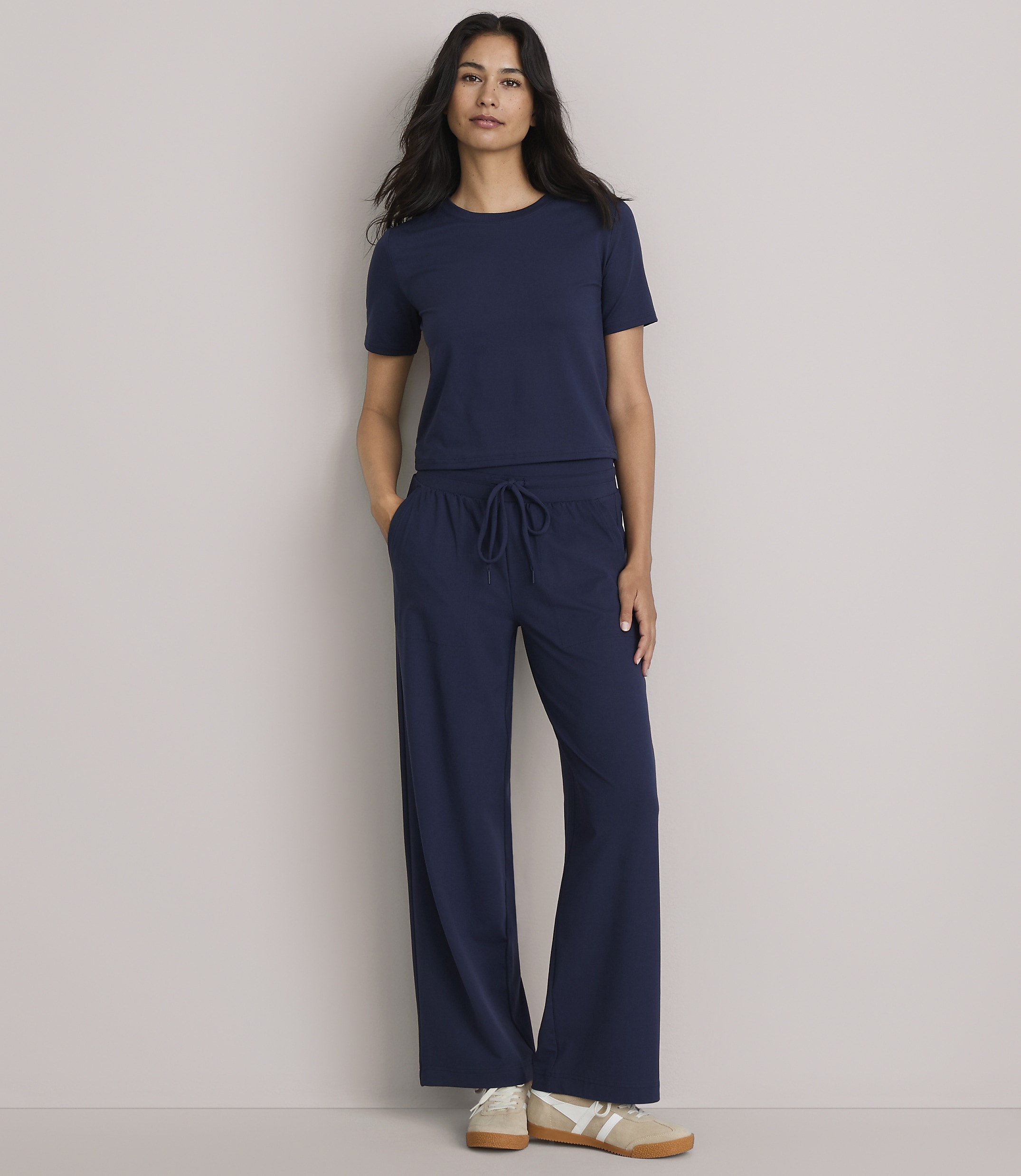A woman in a navy blue t-shirt and wide-leg pants stands against a plain gray background.
