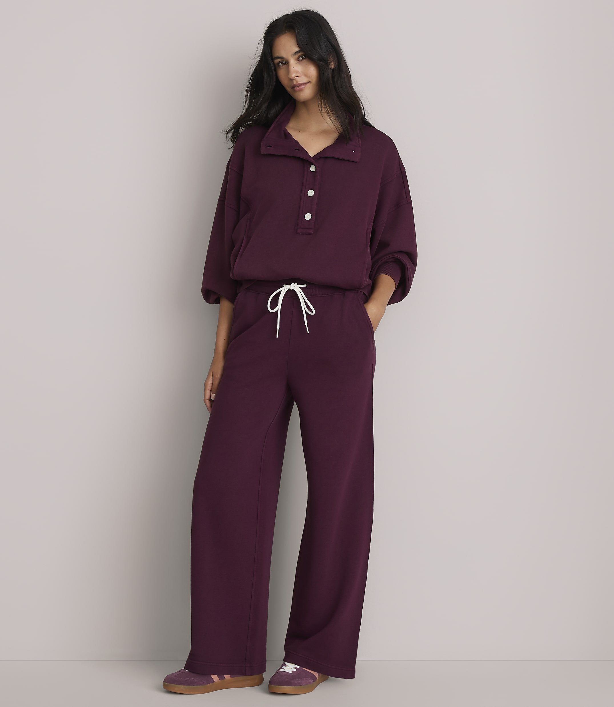 A woman in a burgundy loungewear set stands against a plain gray background.