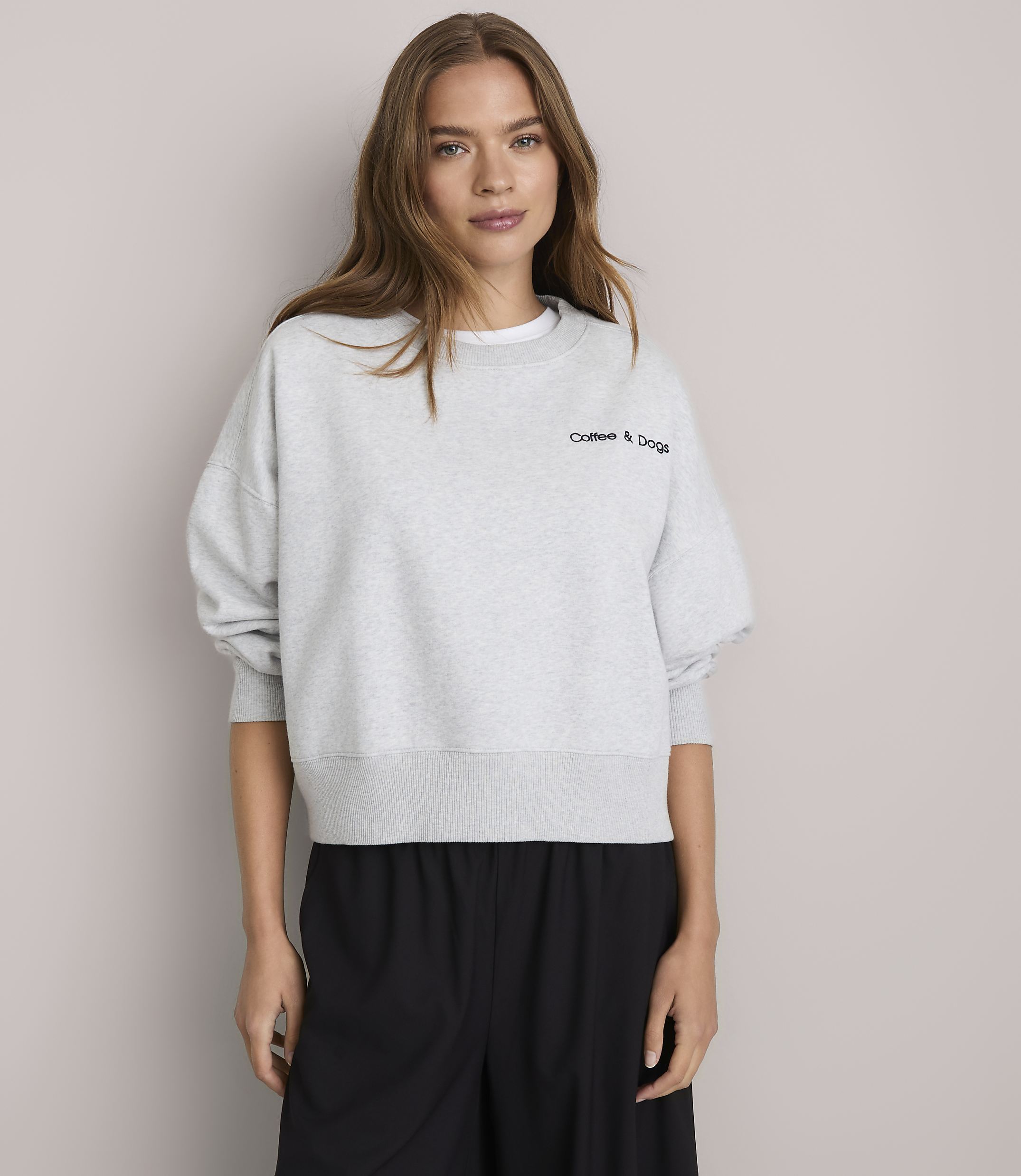 A young woman in a light gray sweatshirt stands against a plain white background.