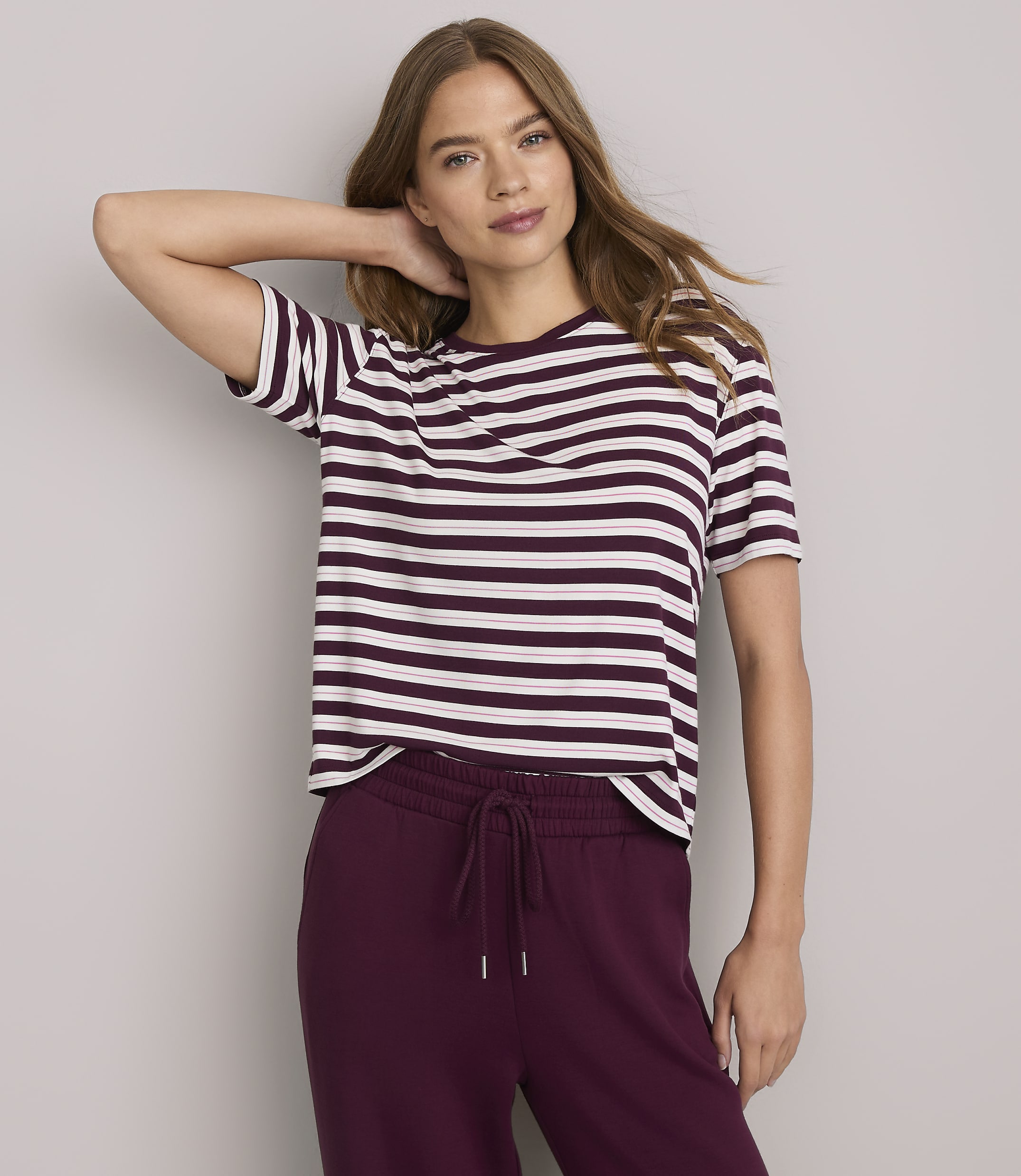 A woman in a striped t-shirt and maroon sweatpants poses against a plain gray background.