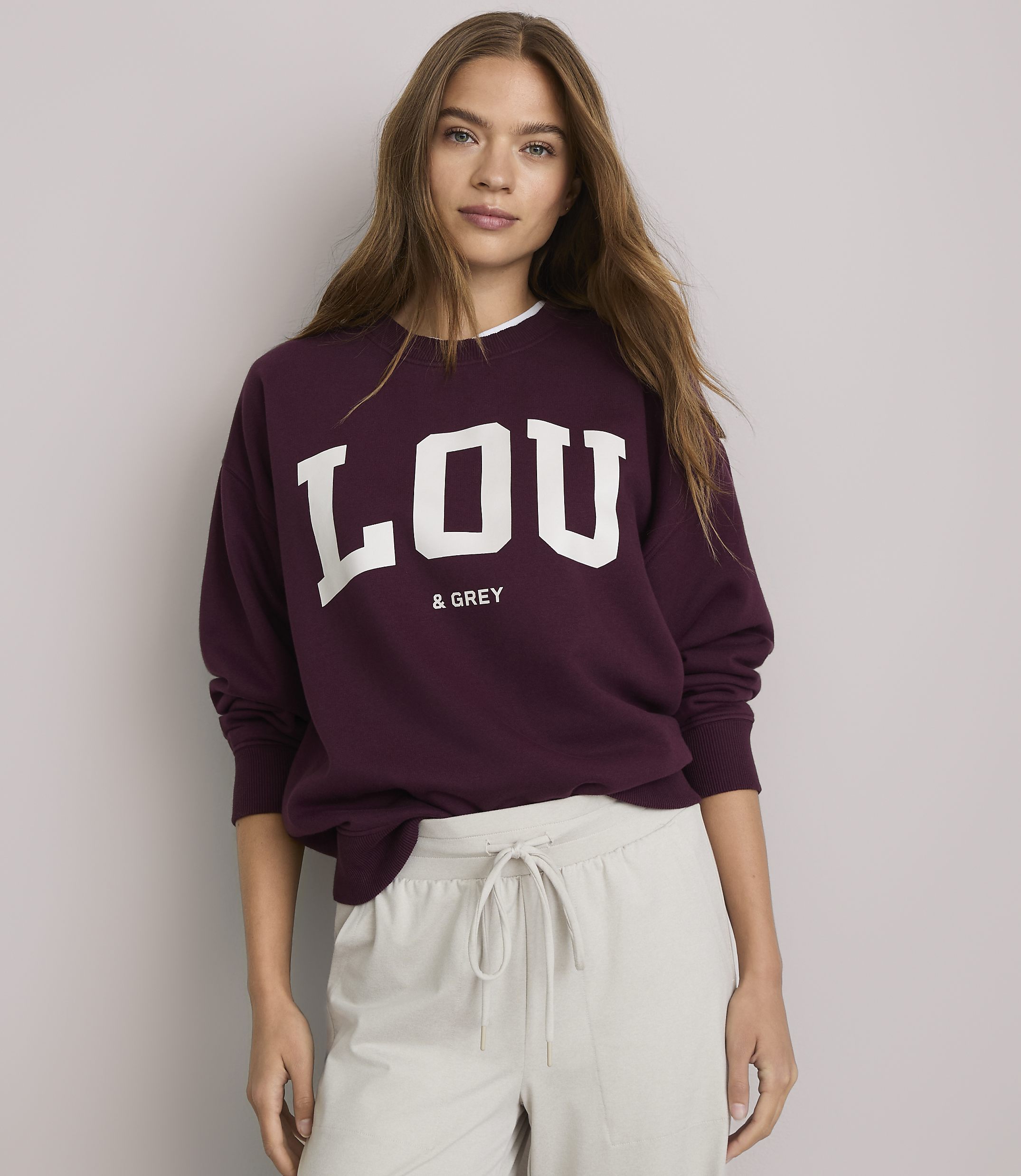 A young woman in a maroon sweatshirt with "LOU & GREY" printed on it stands against a plain white background.