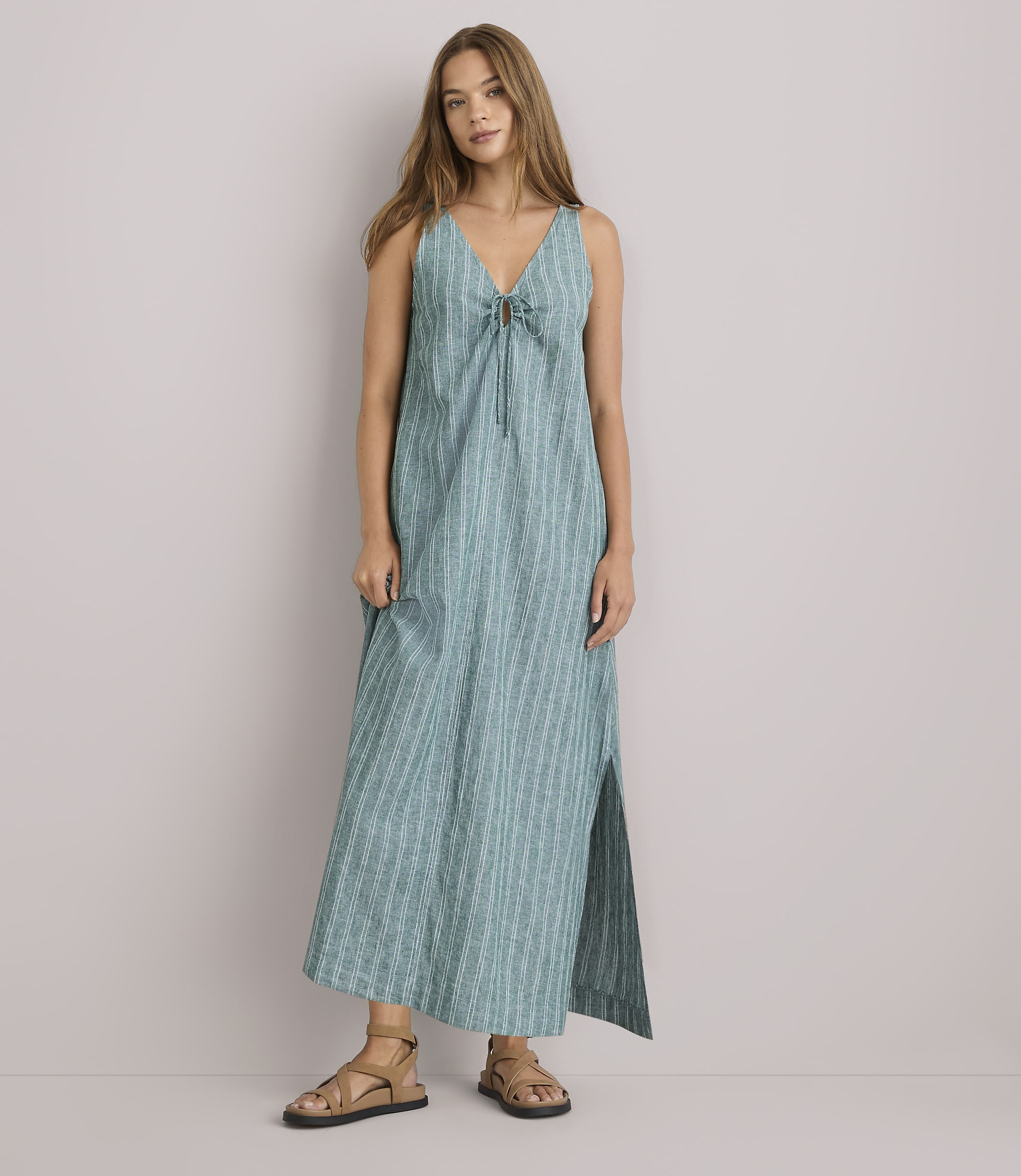 A young woman in a green striped dress stands with her arms crossed against a plain white background.