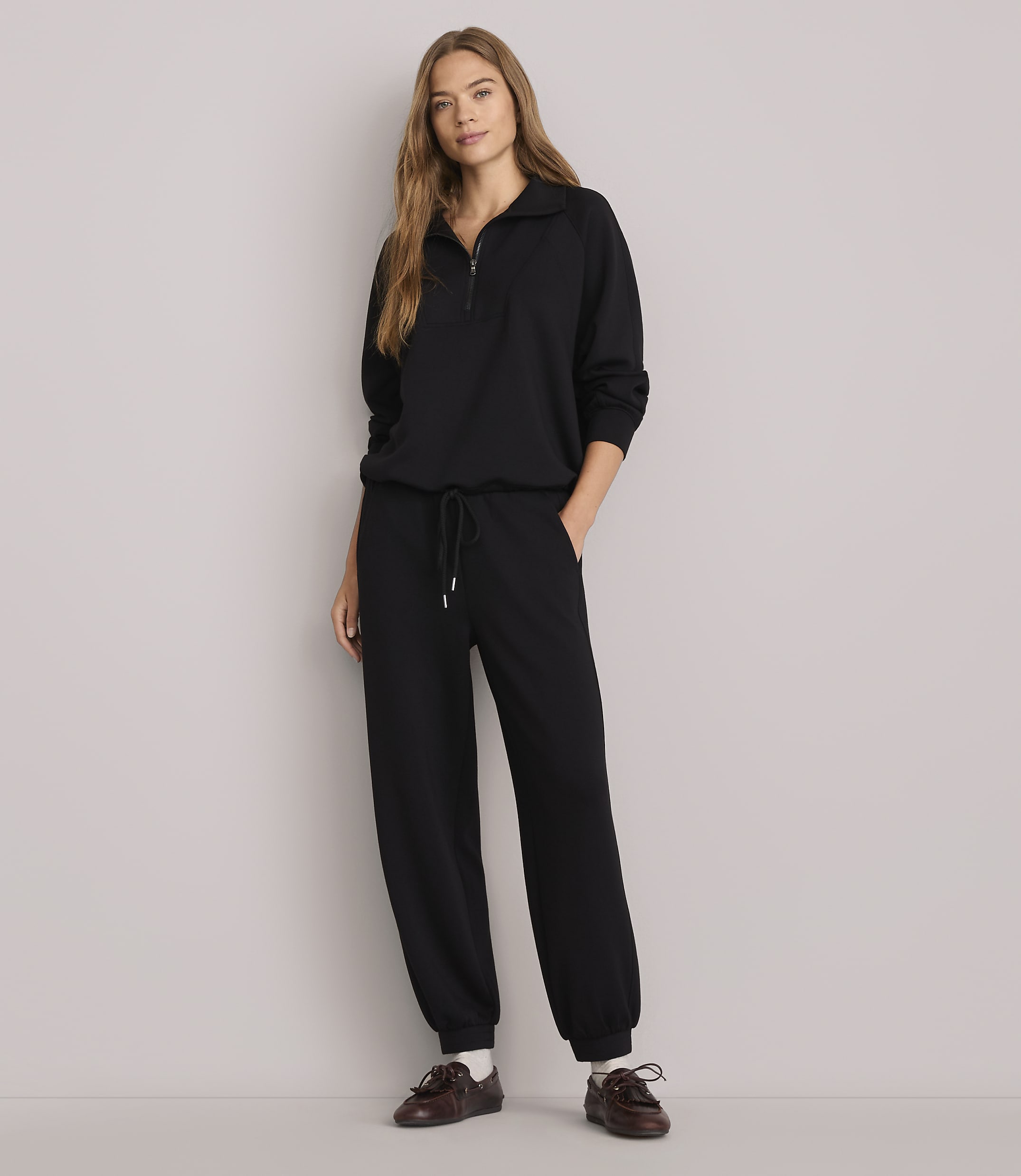 A woman in a black tracksuit stands against a plain white background.