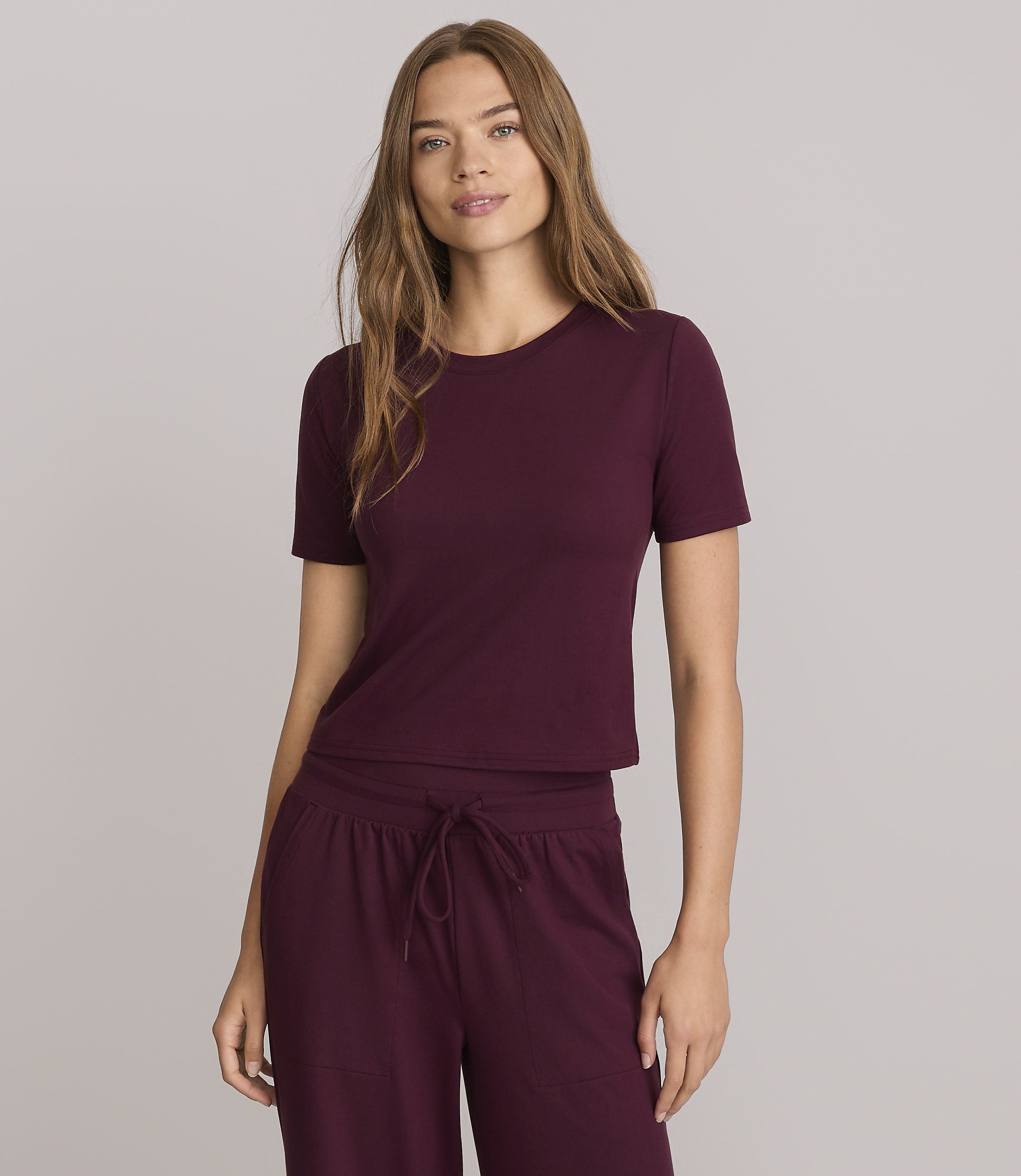 A woman in a maroon t-shirt and matching pants stands against a plain gray background.