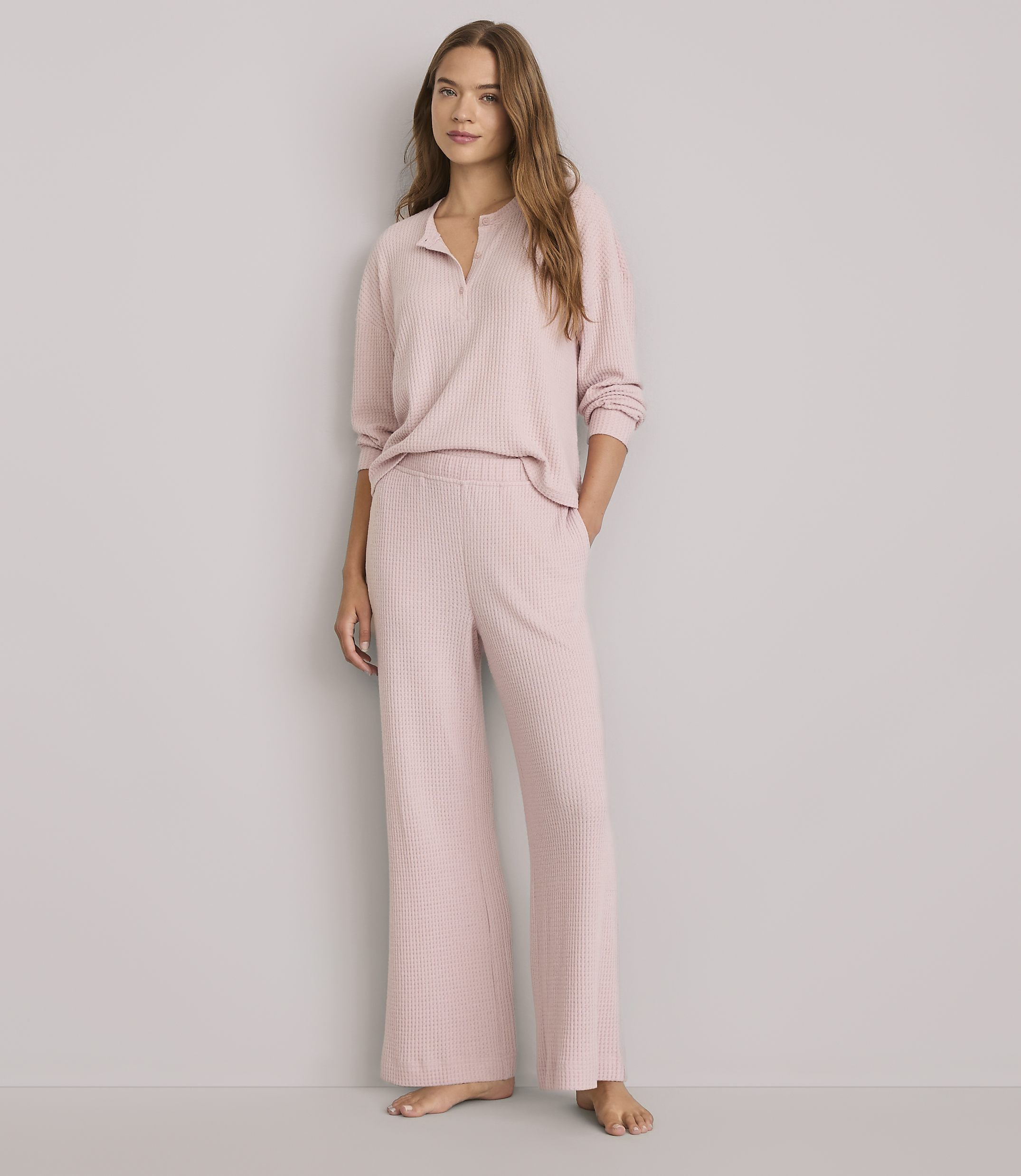 A woman in a pink pajama set stands against a plain gray background.