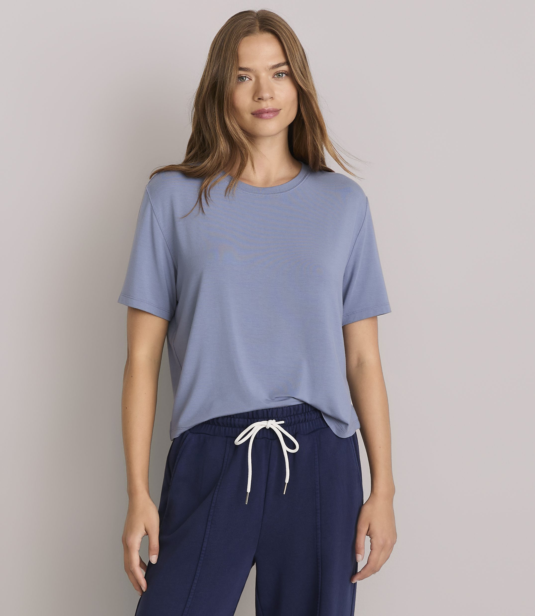 A woman in a blue t-shirt and navy pants stands against a plain gray background.