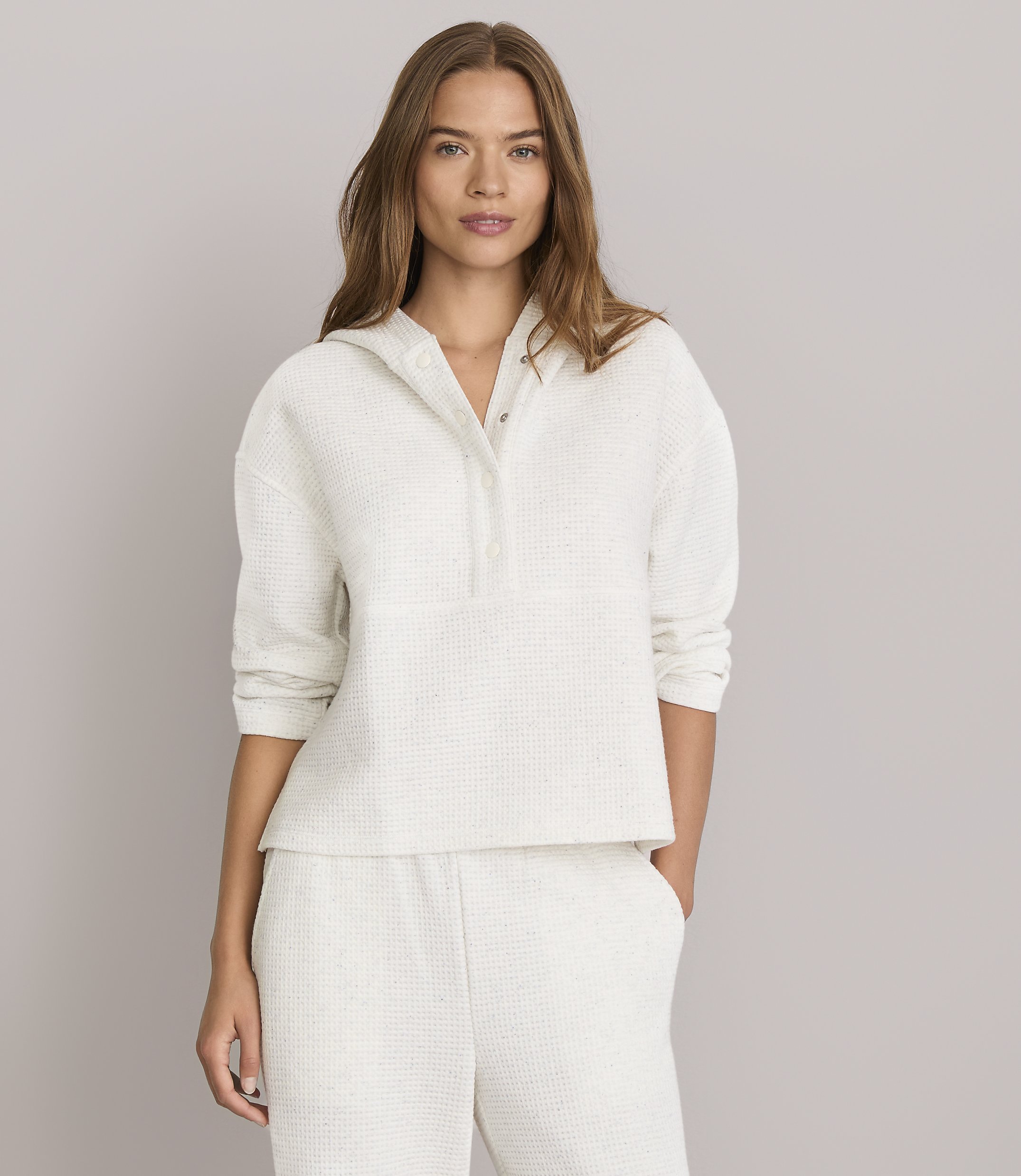 A woman in a cream waffle-knit hoodie and matching pants stands against a plain gray background.
