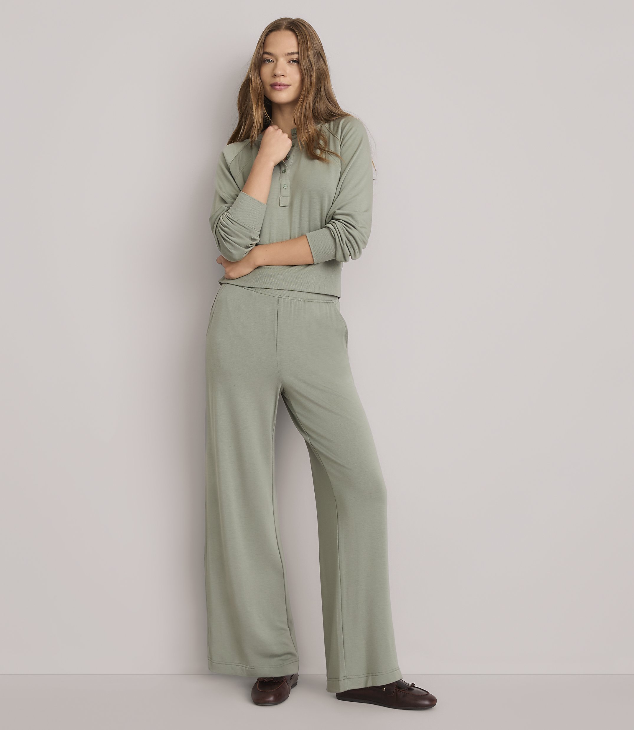 A young woman in a sage green loungewear set stands against a plain white background.