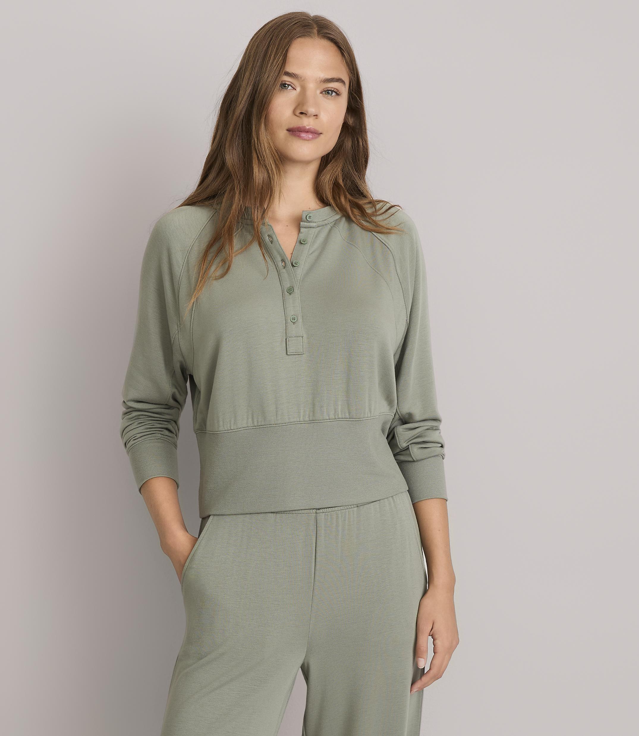 A woman in a green henley shirt and matching pants stands against a plain gray background.