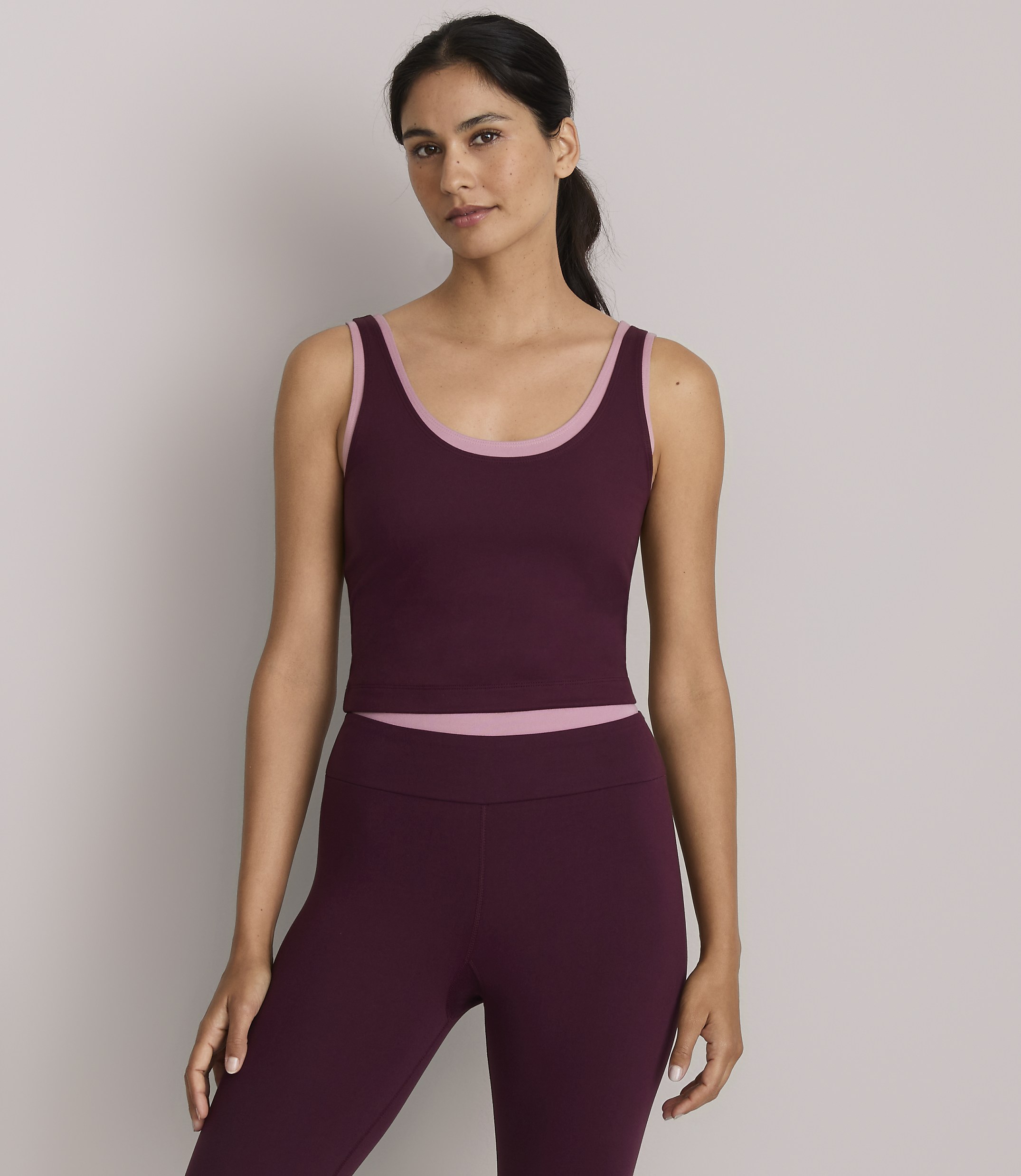 A woman in a burgundy crop top and leggings stands against a plain gray background.