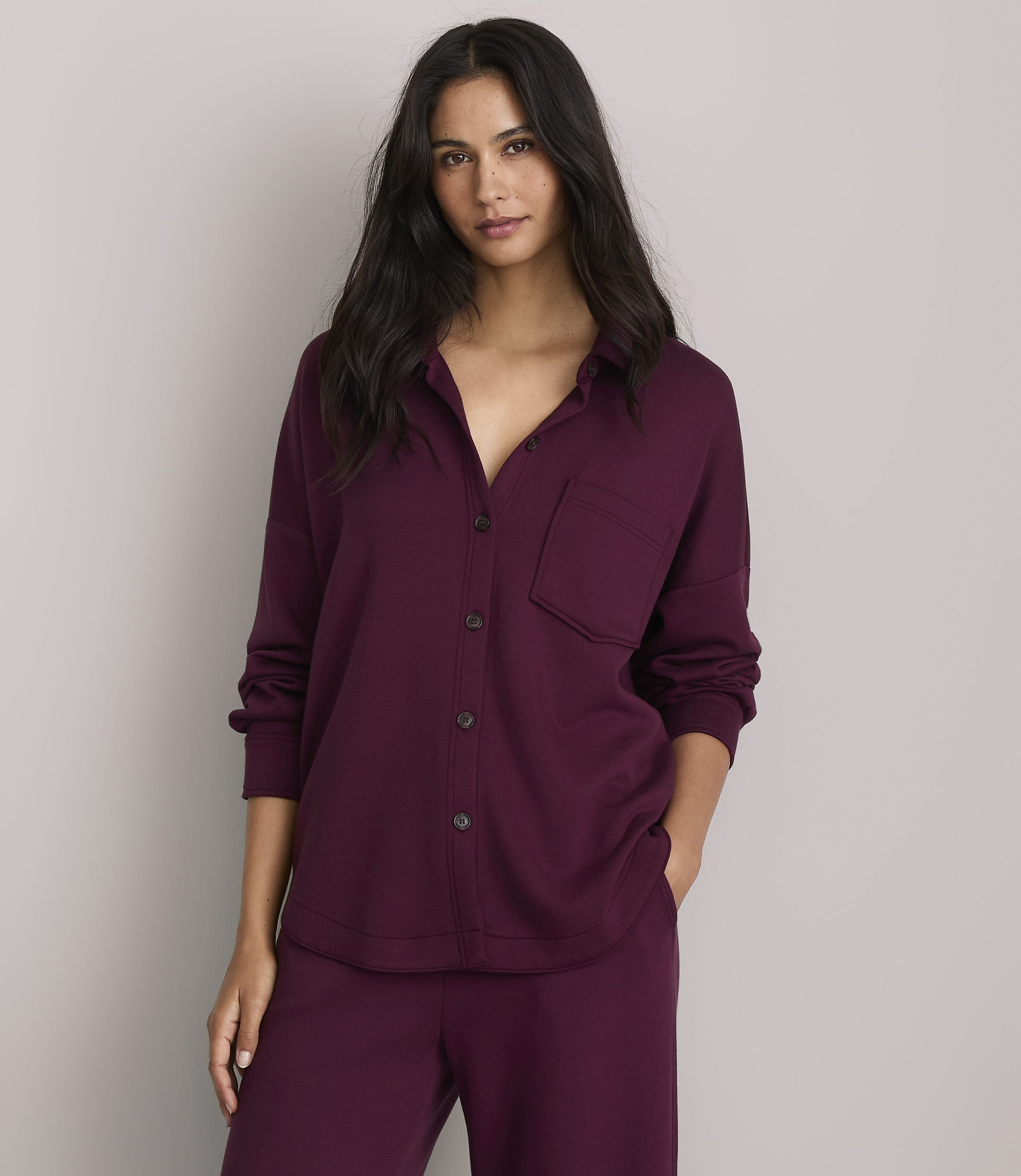 A woman in a burgundy pajama set stands against a plain gray background.