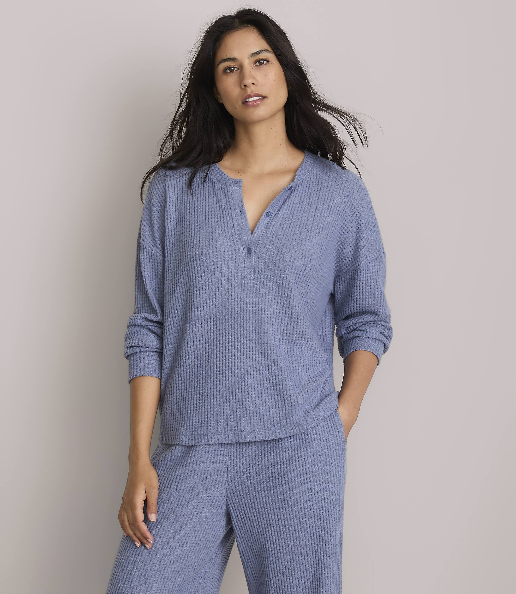 A woman in a blue waffle-knit top and pants stands against a plain gray background.