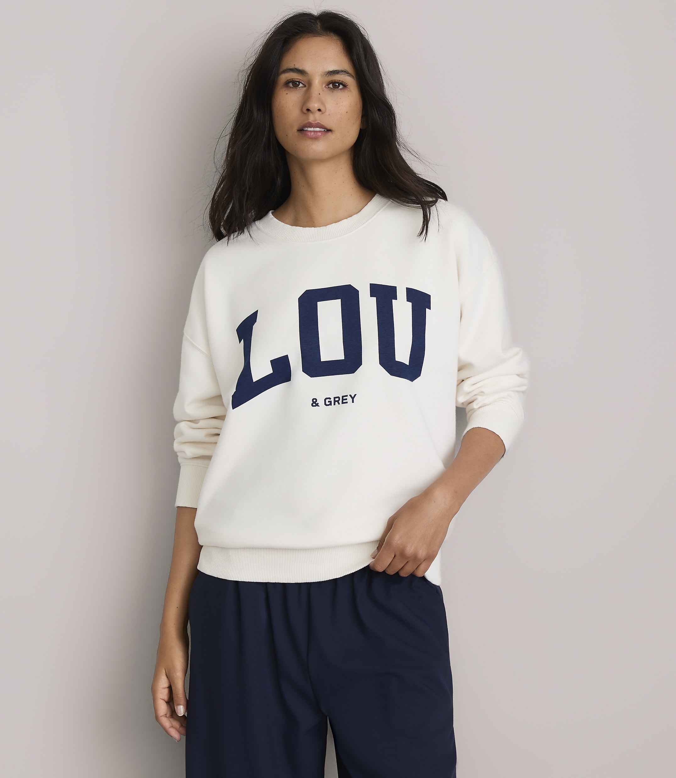 A woman in a cream sweatshirt with "LOU & GREY" printed on it stands against a plain, light gray background.