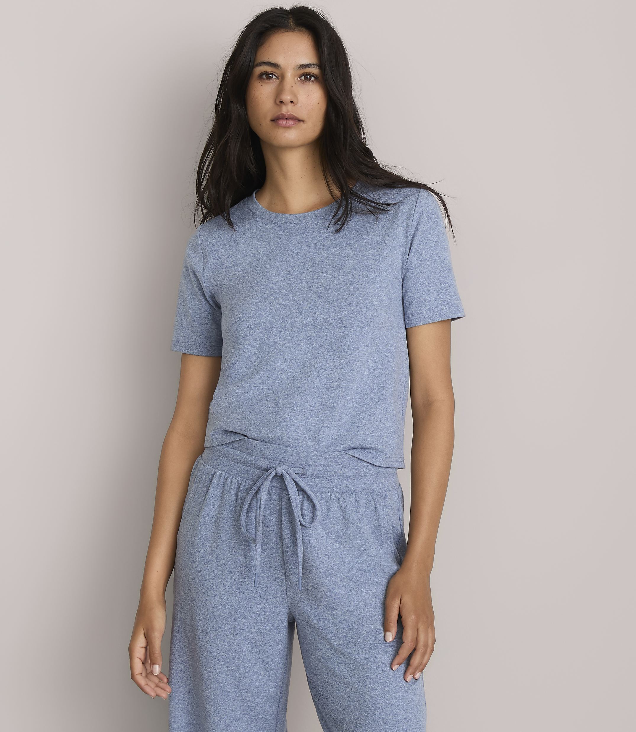 A woman in a blue t-shirt and matching pants stands against a plain gray background.