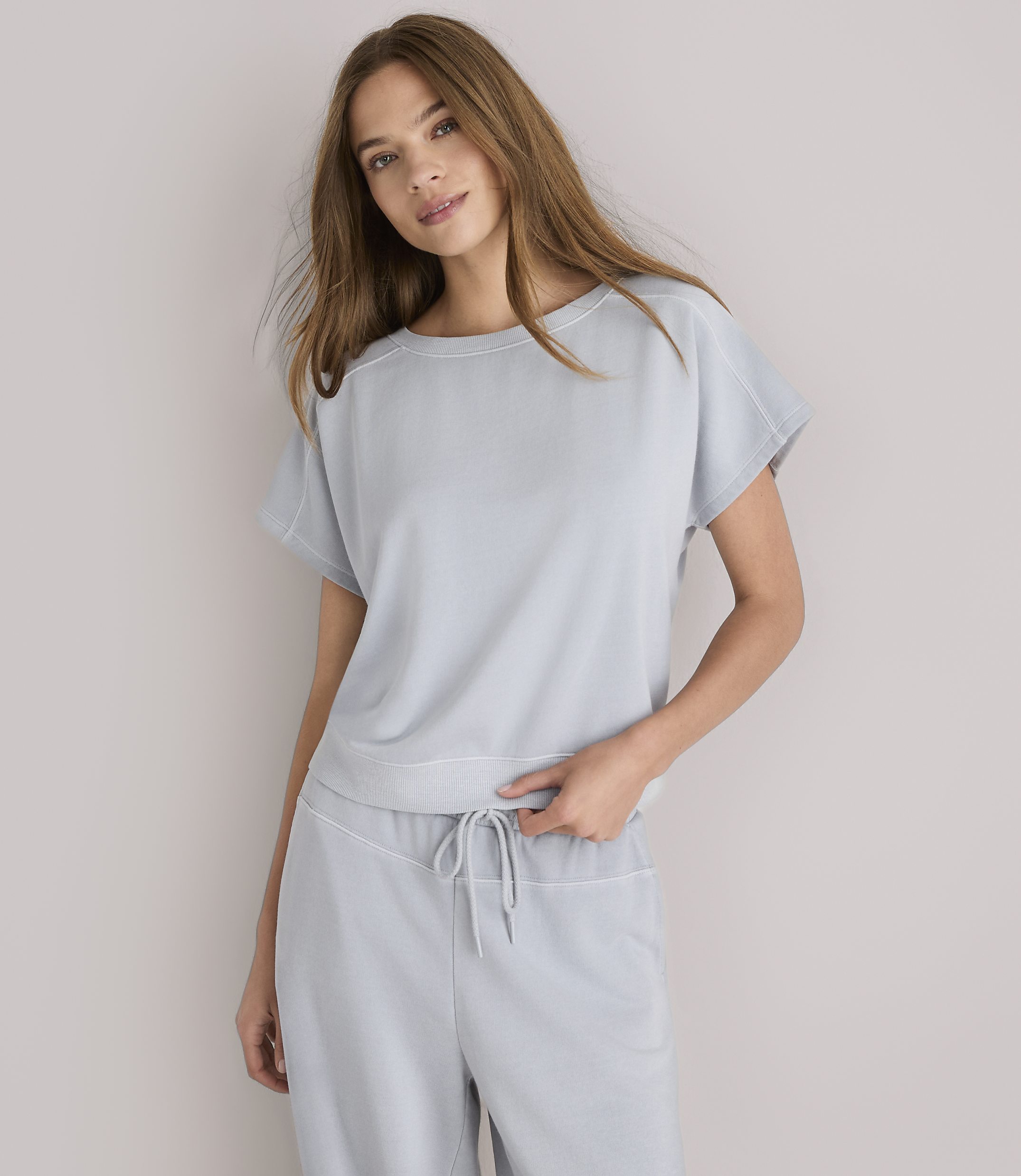 A woman in a light gray loungewear set stands against a plain white background.