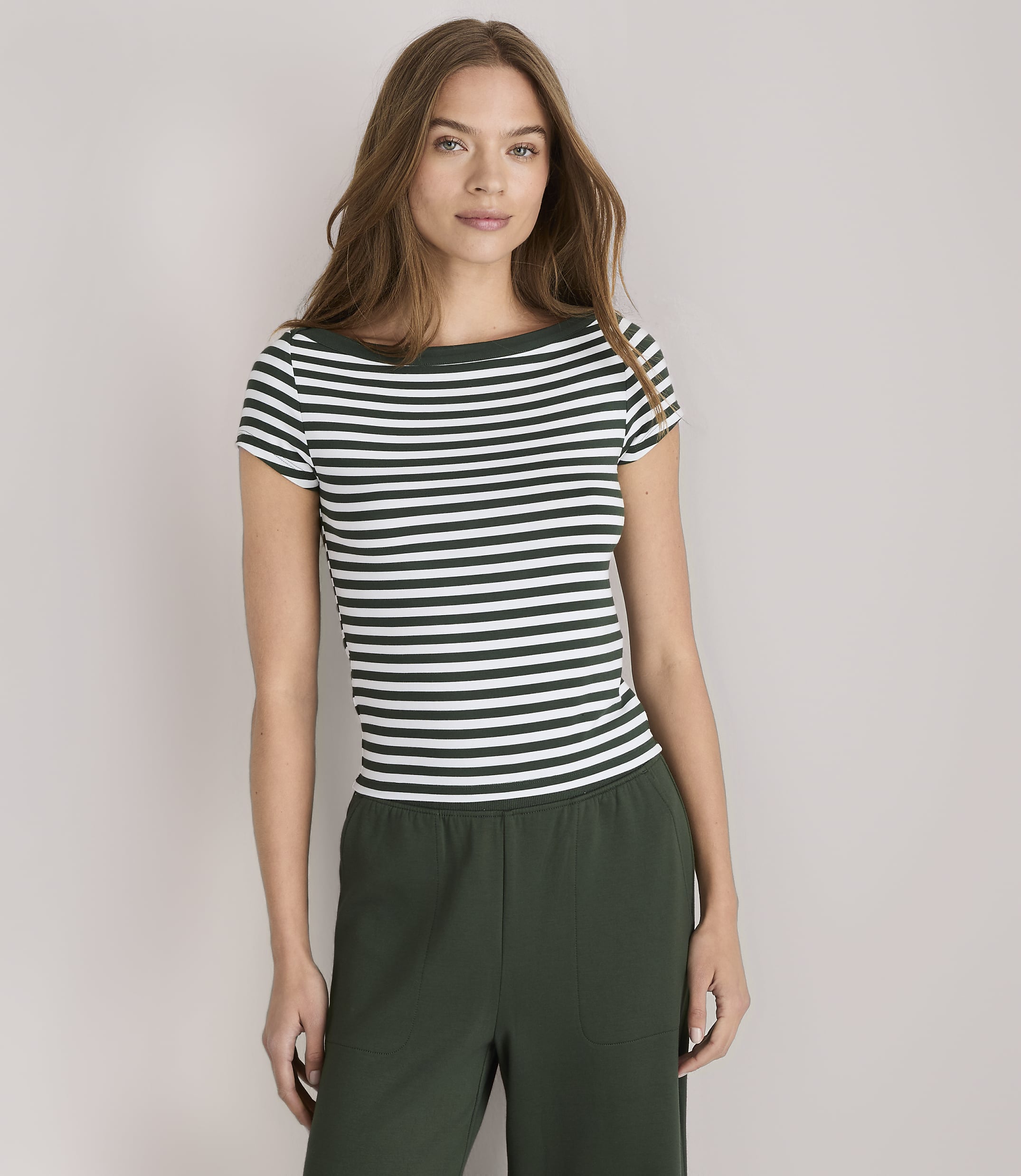 A woman in a striped shirt and green pants stands against a plain white background.
