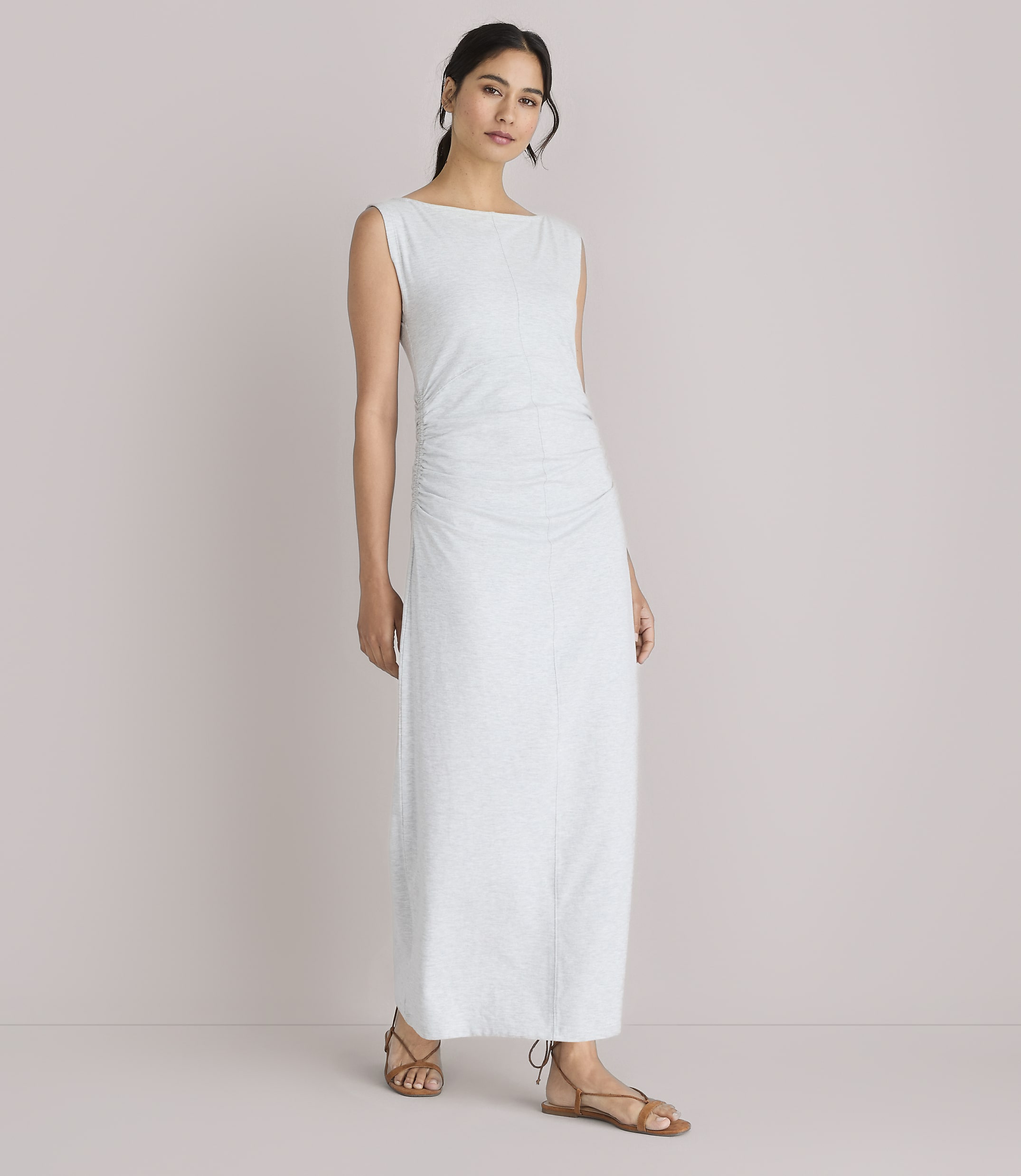 A woman in a light-colored, ruched maxi dress stands against a plain white background.