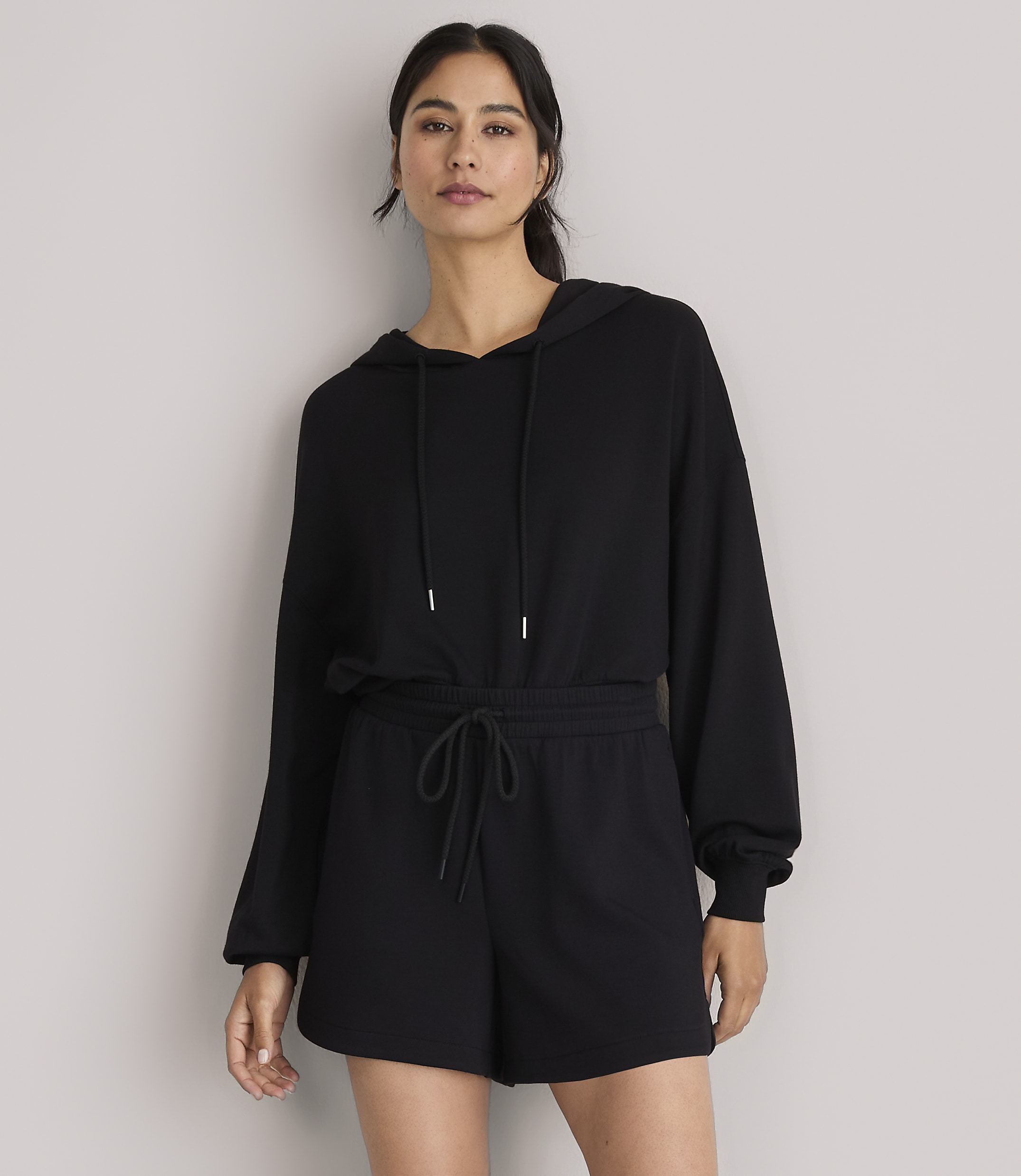 A woman in a black hoodie and shorts stands against a plain white background.
